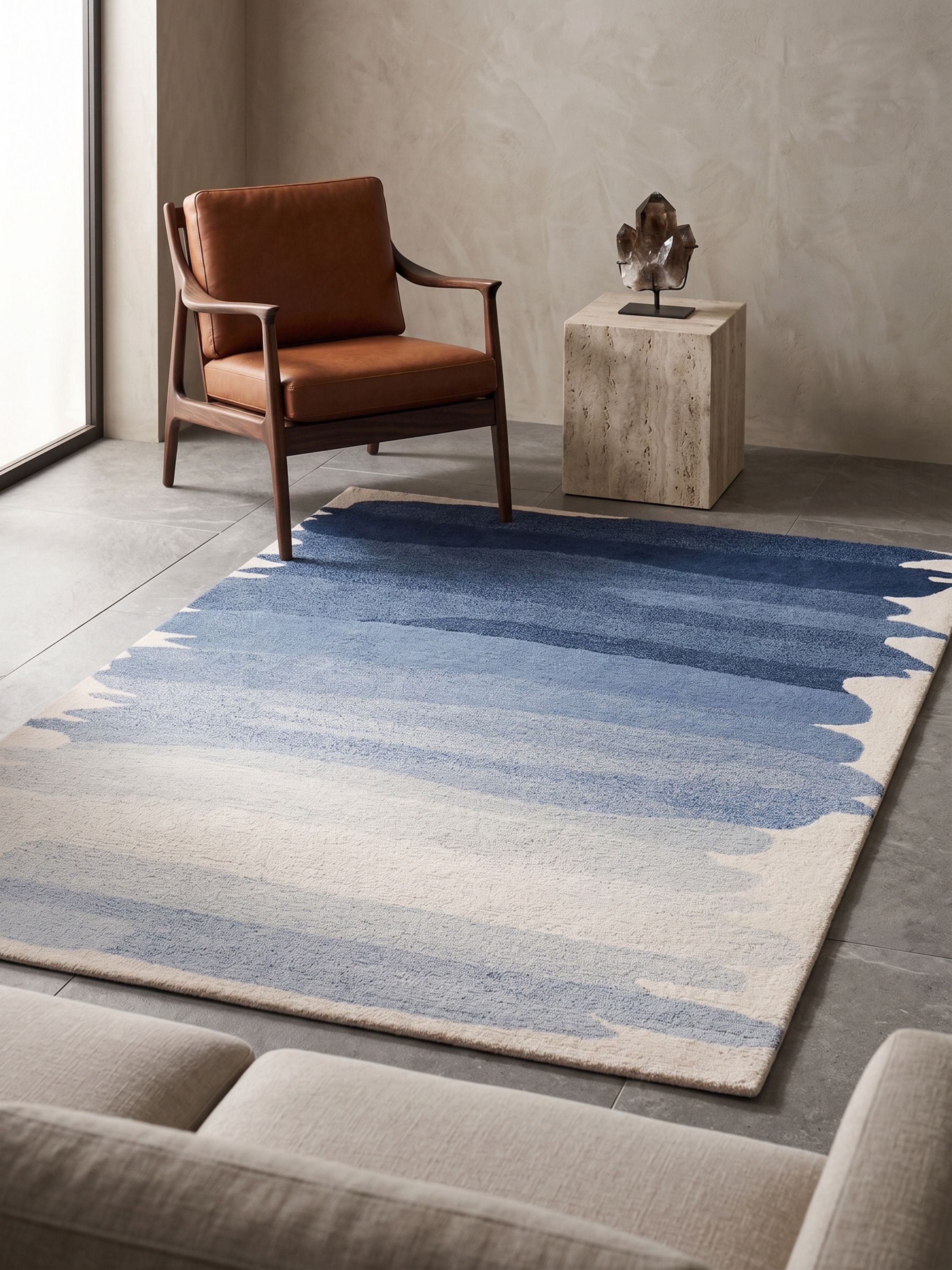 Abstract blue gradient wool area rug with brushstroke edges placed in a modern interior with chair and stone pedestal