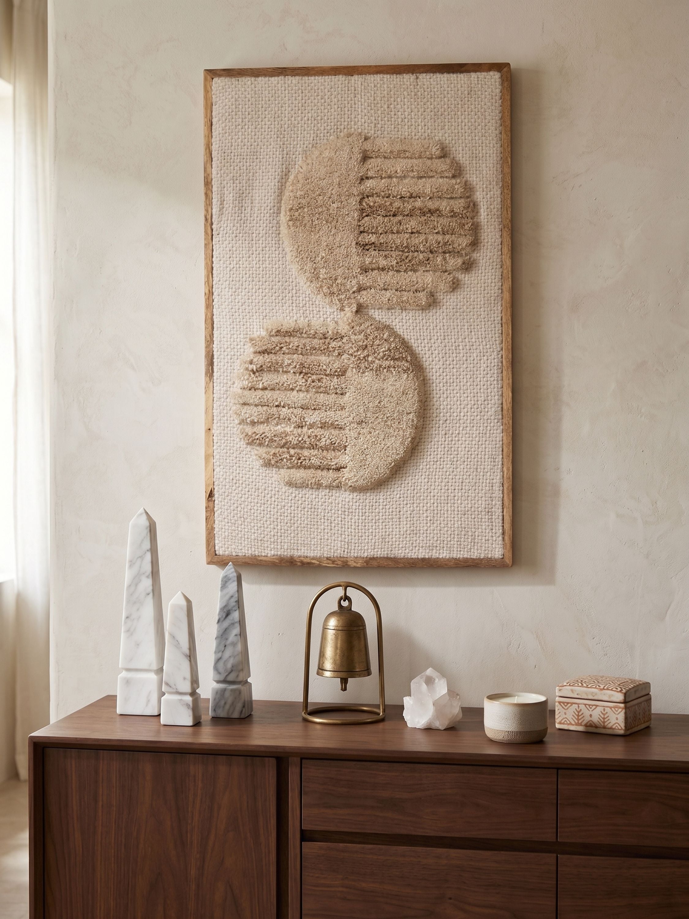 Tufted wool wall art with layered circular texture in ivory and beige tones, styled above a wooden cabinet with sculptural decor objects
