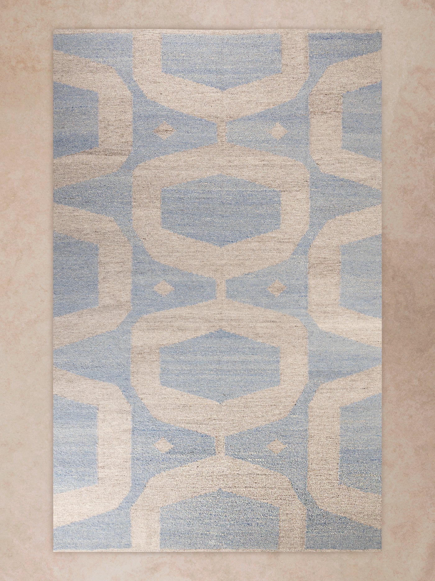 Handwoven area rug with geometric pattern in soft blue and beige tones shown in motion, with shifting light revealing woven texture, tonal variation, and surface depth