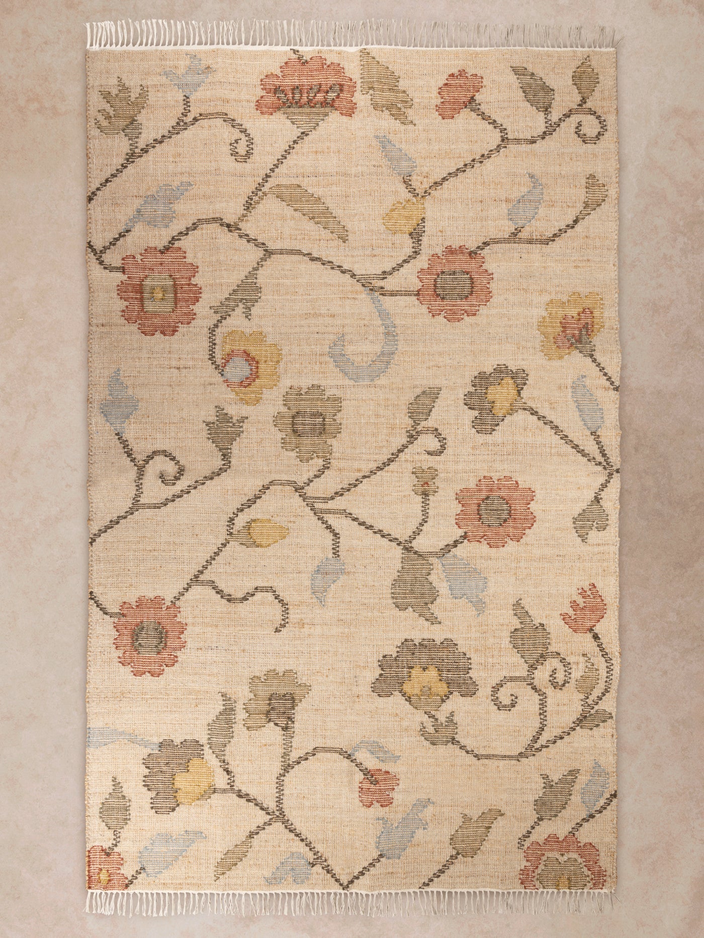 Handwoven floral area rug in beige and muted tones shown in motion, with shifting light revealing weave texture, fringe detail, and soft color variation