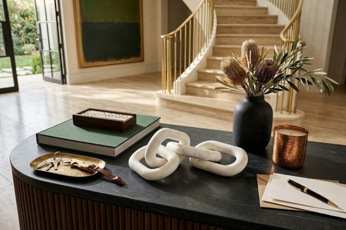 White marble chain links resting on a dark stone entry console beside a brass tray of keys and a lit candle