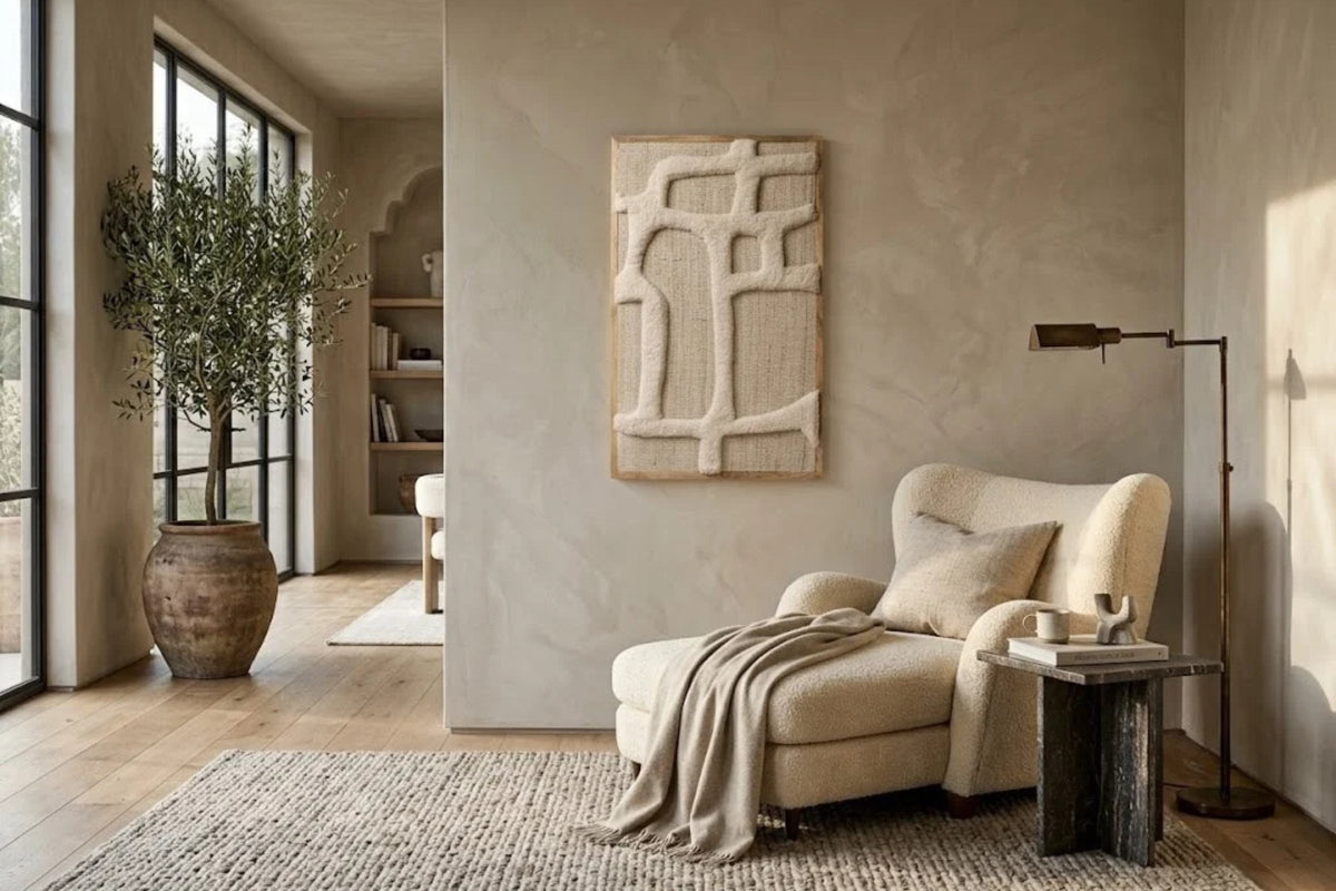 Ivory wool wall panel with raised linear forms, hung above a cream reading chair and a dark stone side table
