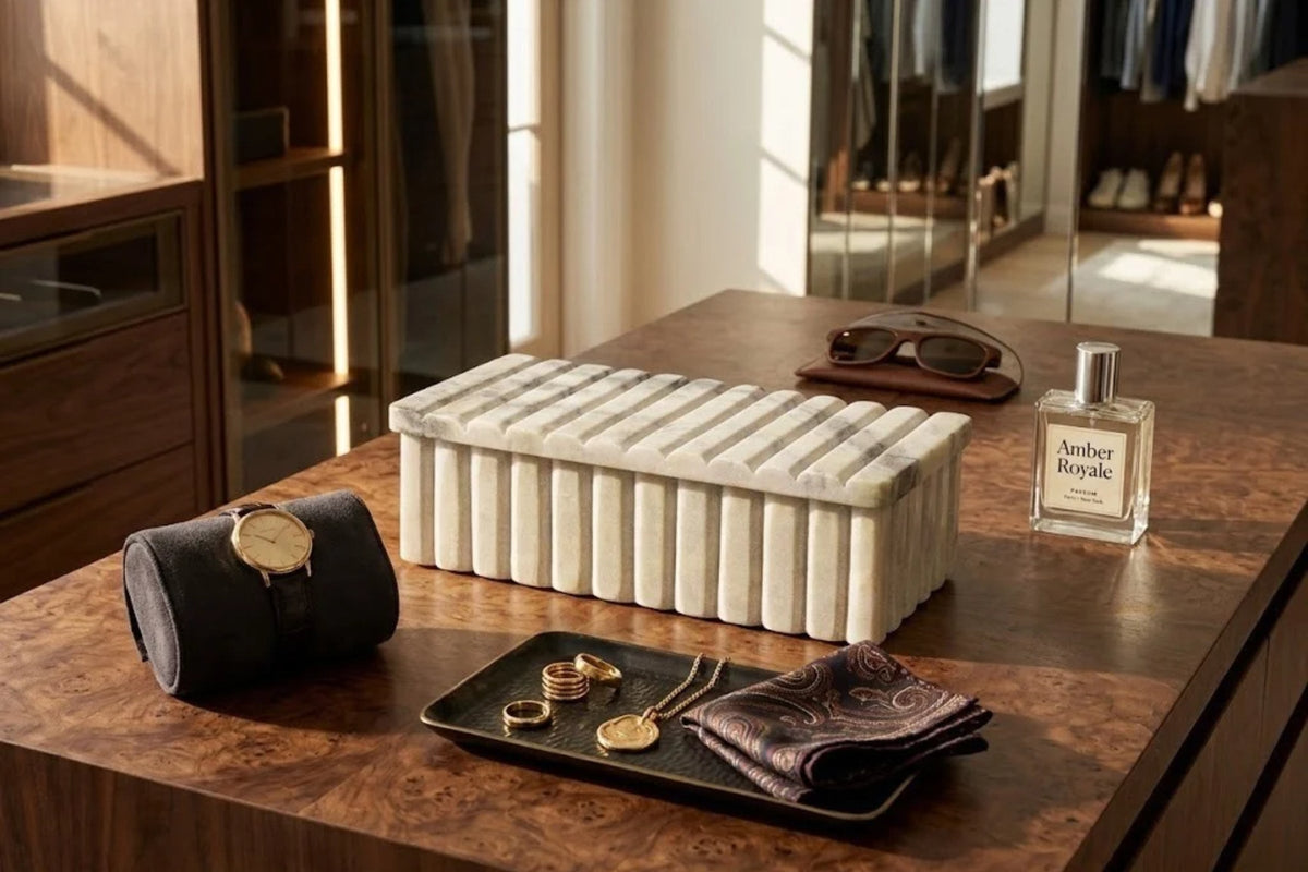 Fluted cream travertine box closed on a burl wood dressing island, watch roll and jewelry tray beside it