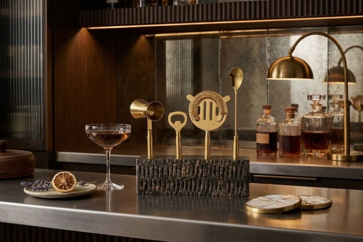 Gold bar tools seated in a chisel-textured onyx stand on a dark bar counter, a cocktail poured alongside