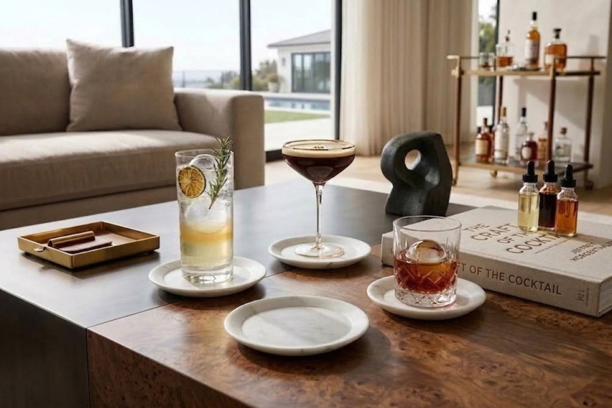 White marble coasters under cocktails on a dark wood coffee table, one empty coaster waiting beside them