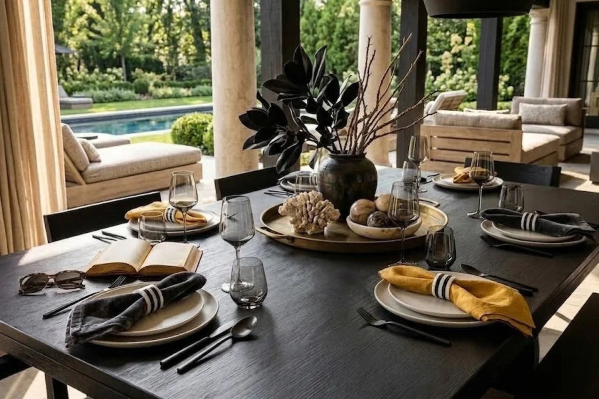 Round brass tray of coral and a stone bowl centered on a dark oak dining table under a garden loggia