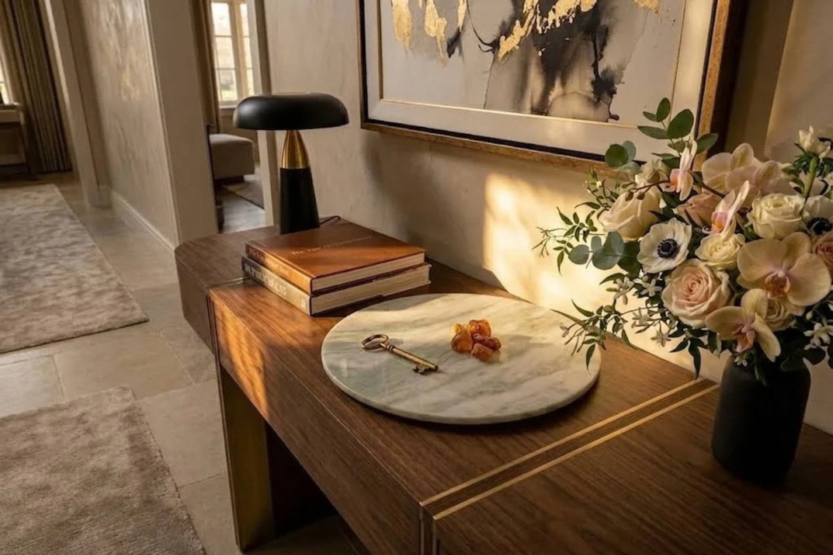 Ivory onyx tray with sage veining holding a single key on an inlaid wood console in a sunlit hallway