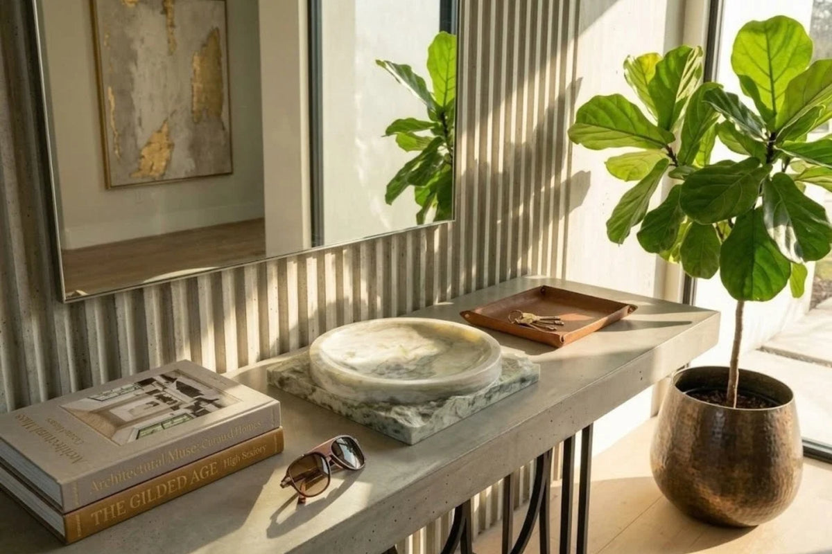 Green onyx bowl on a chiseled base, resting on a gray console table beside a leather tray in low afternoon sun