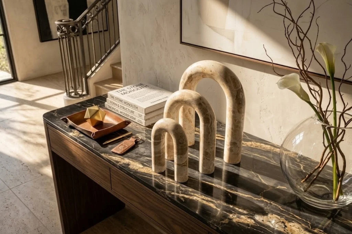 Three cream onyx arches in graduated heights standing on a dark veined marble console in an entry hall