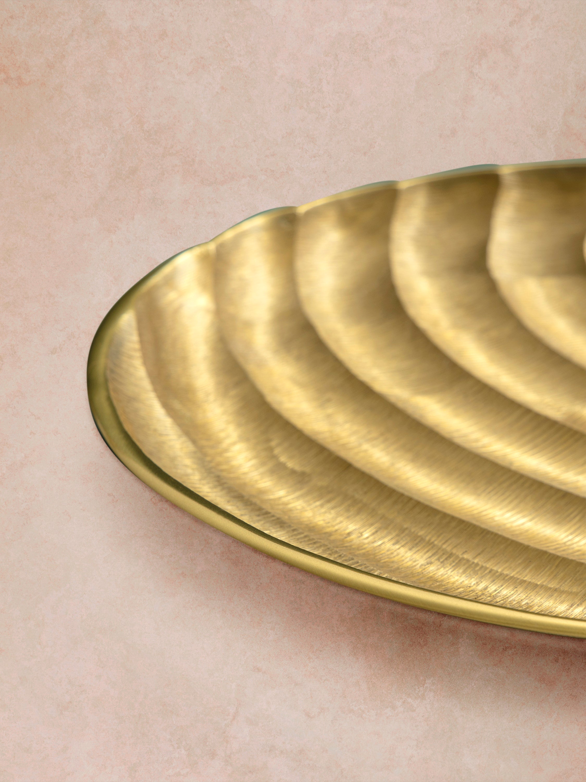 Close-up of gold tray showing curved edge profile, layered ridges, and smooth metallic finish across the textured surface