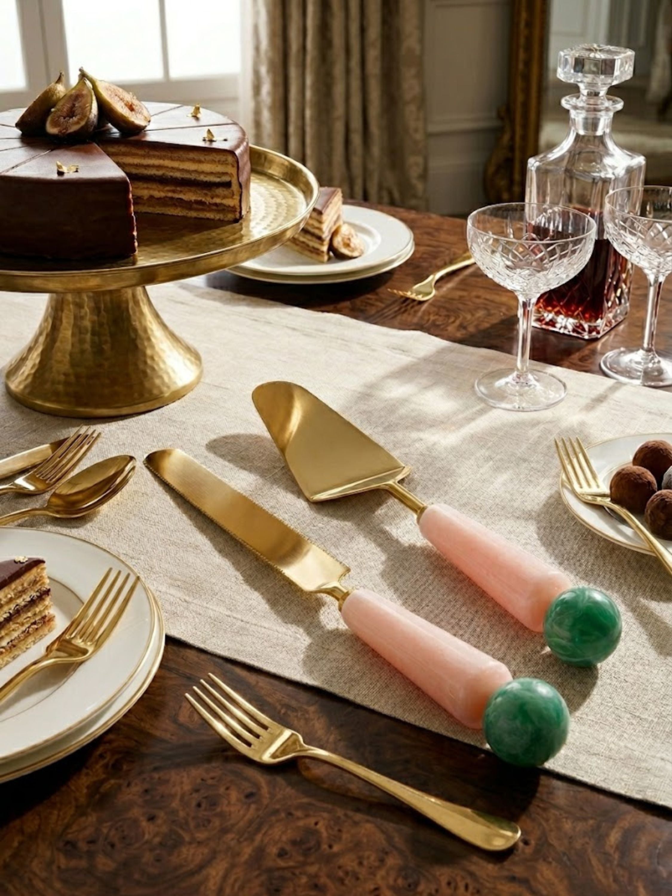 Copenhagen cake serving set displayed on a dining table with crystal glassware and a layered cake, its pink handles visible.