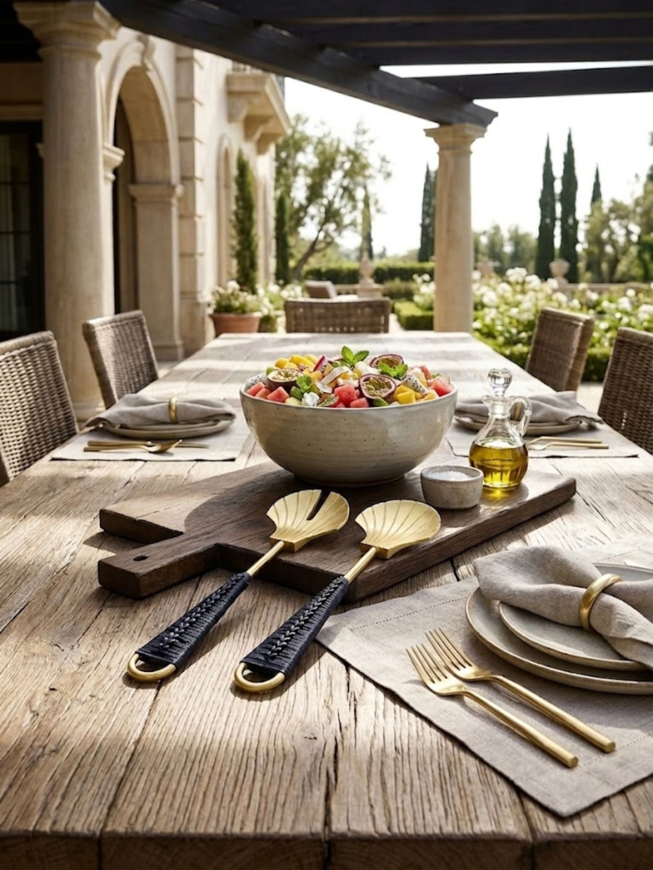 Vitali brass and rattan salad servers displayed on a rustic dining table with fresh fruit salad and linen accents, capturing relaxed poolside entertaining.