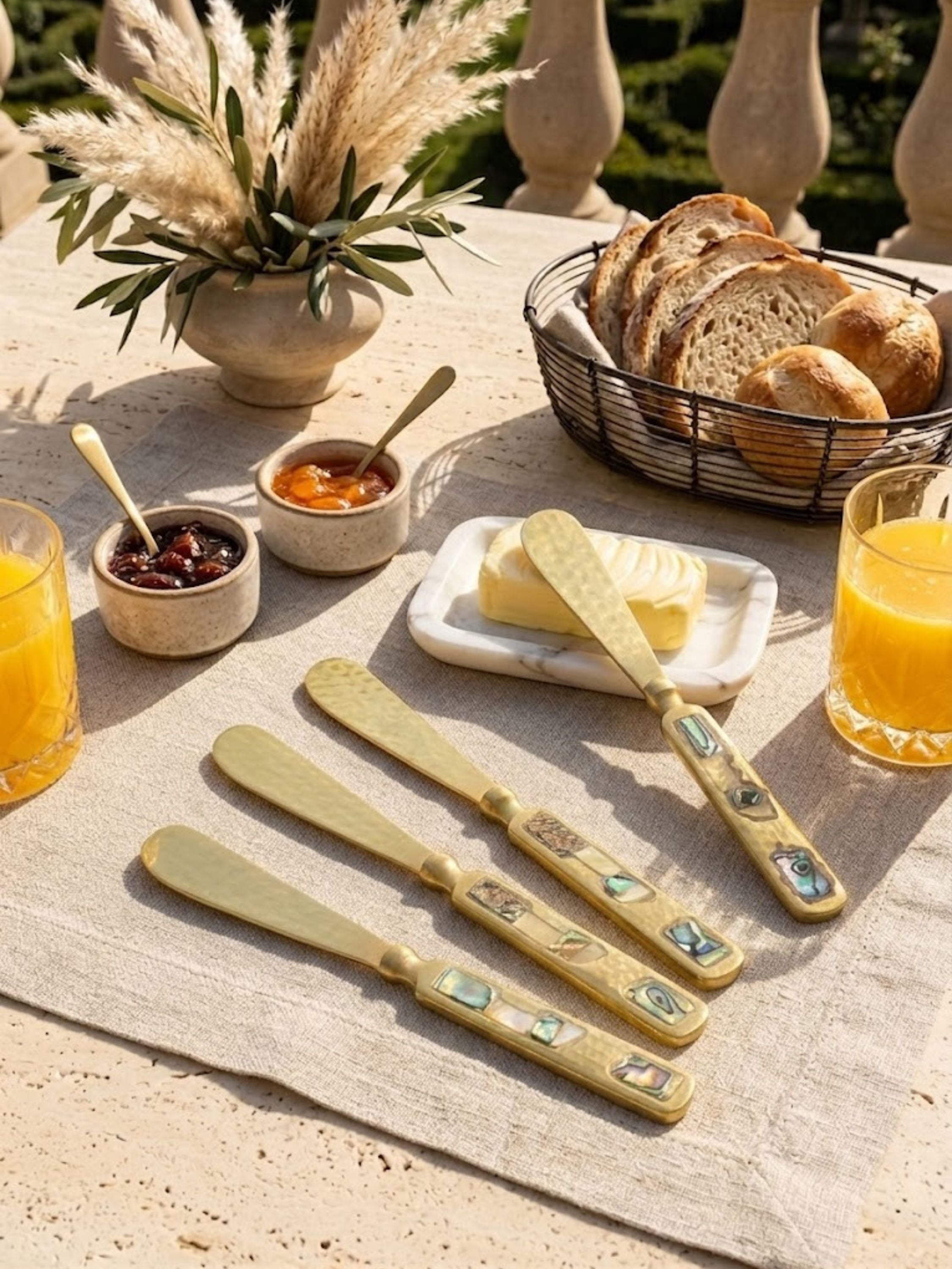 Sisley gold butter knife resting on a marble butter tray with preserves and fresh bread, creating an elevated setting for artisanal breakfast service.