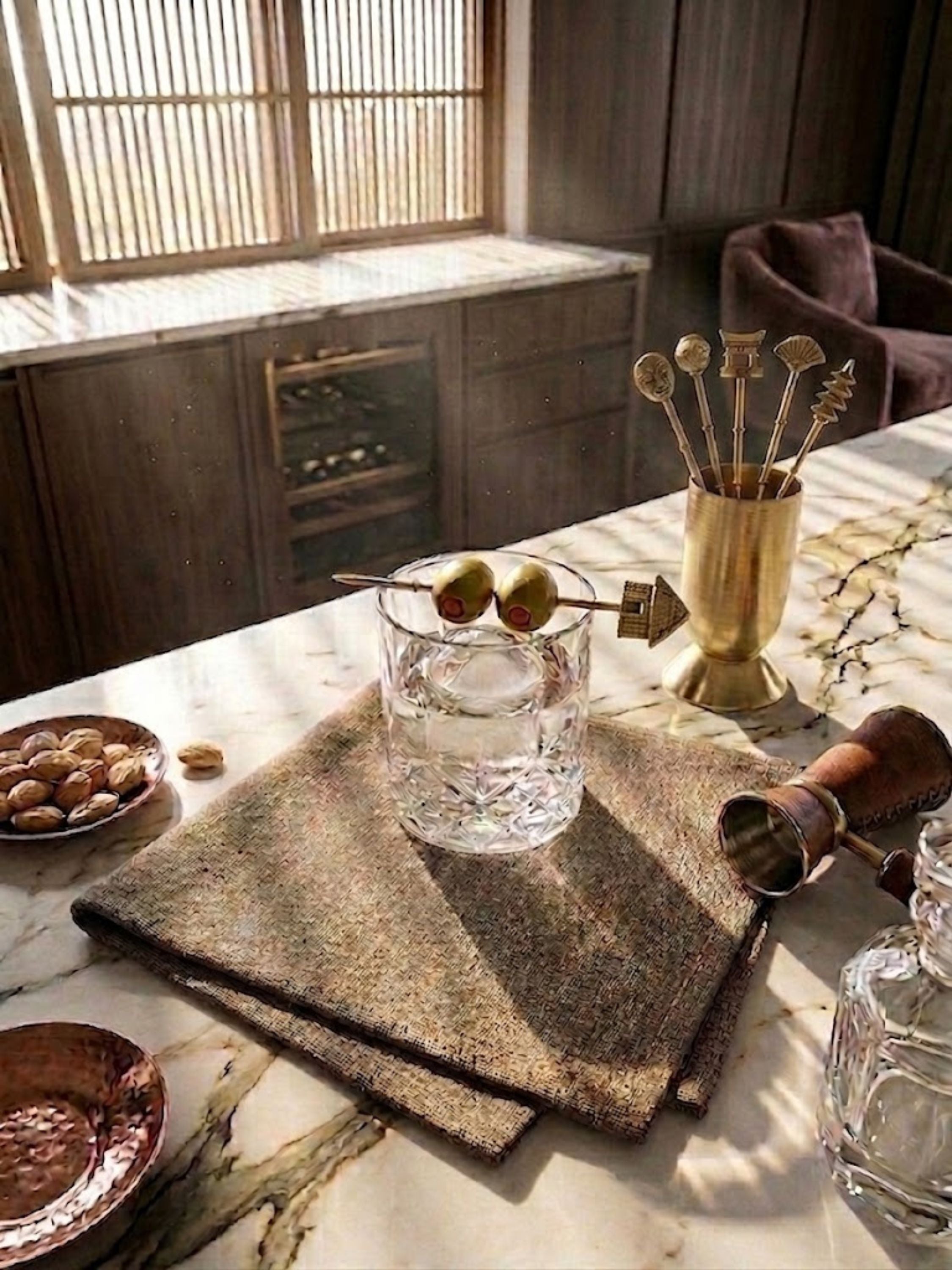 Magnolia gold cocktail picks presented with crystal glassware and spirits, bringing sculptural detail to a curated home bar.