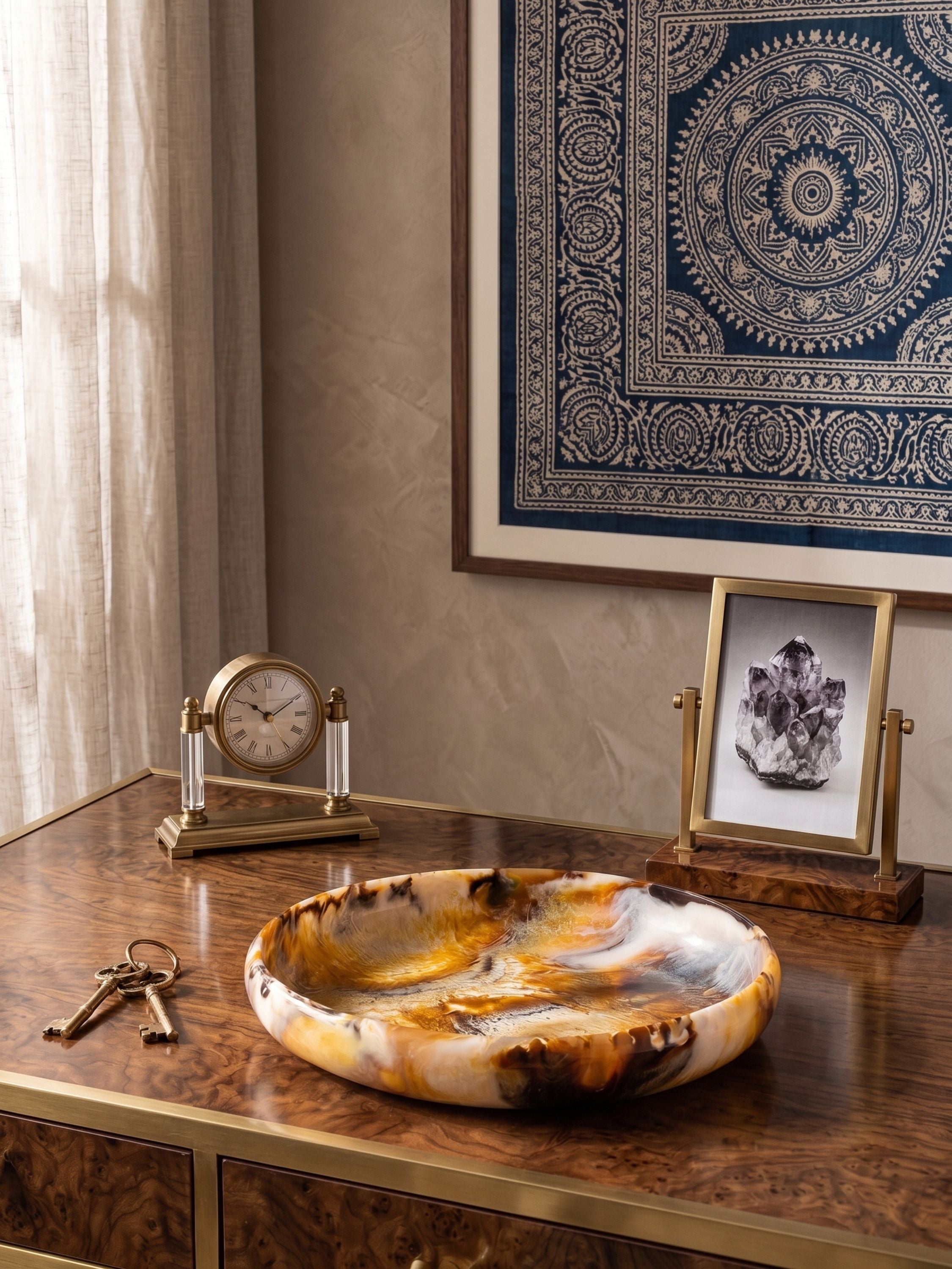 Amber swirl resin decorative bowl styled on a wooden console table with keys and decor objects in a warm, curated interior setting