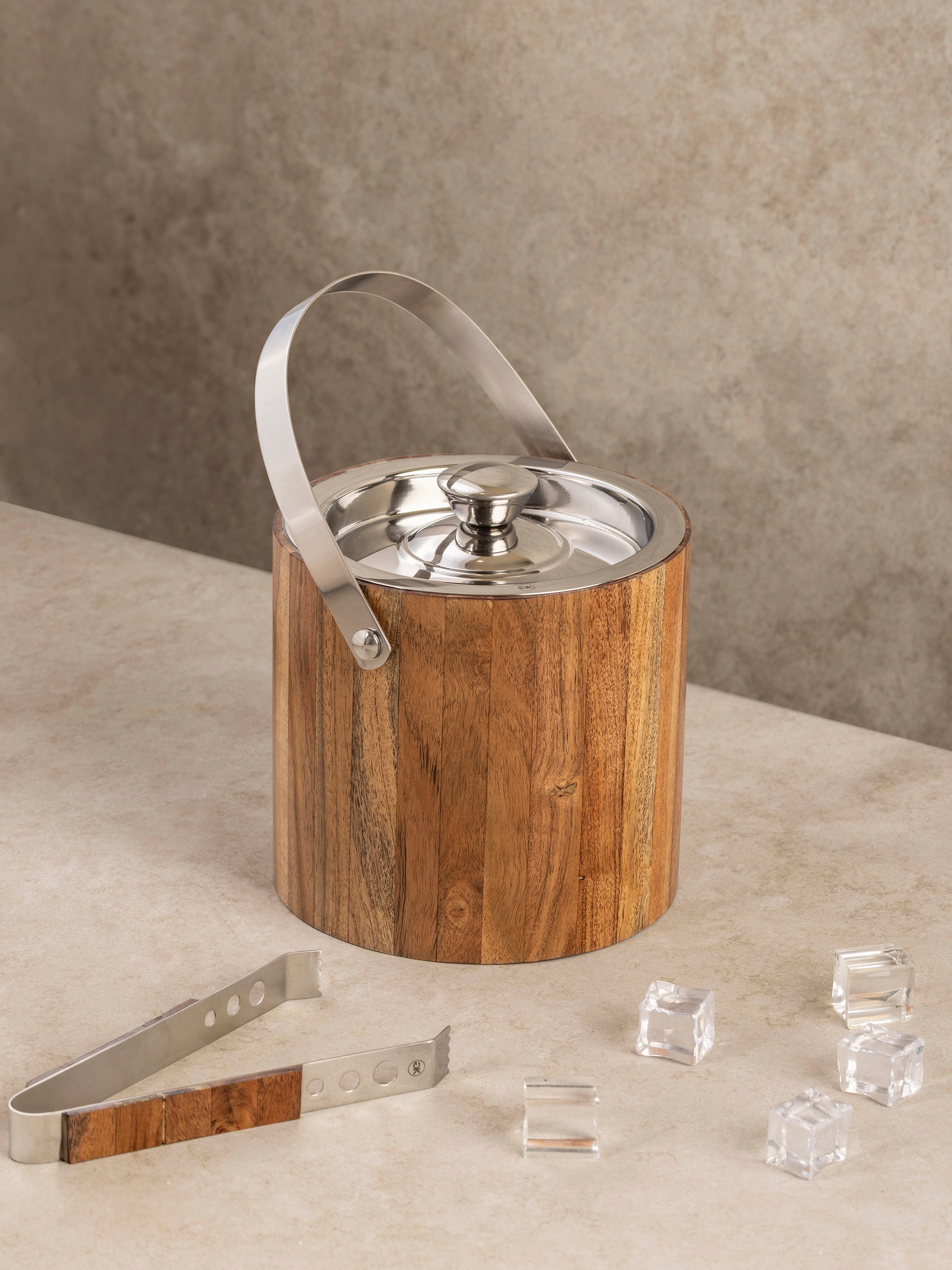 Stainless steel ice bucket with handcrafted wood exterior, fitted lid, and matching tongs, shown in a clean front-facing composition