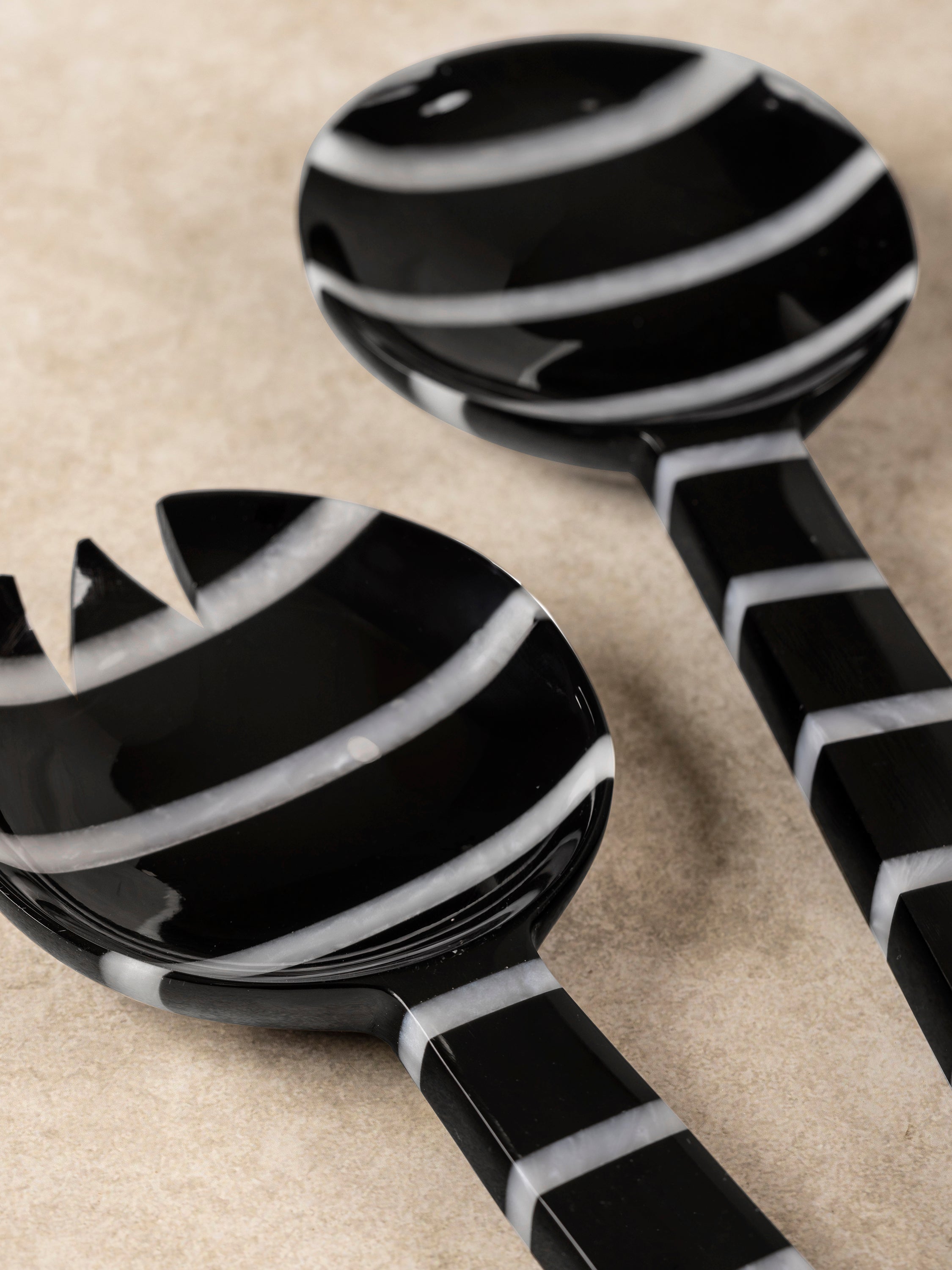 Close-up of Cox salad server handle showing bold black and white stripe pattern and smooth polished finish