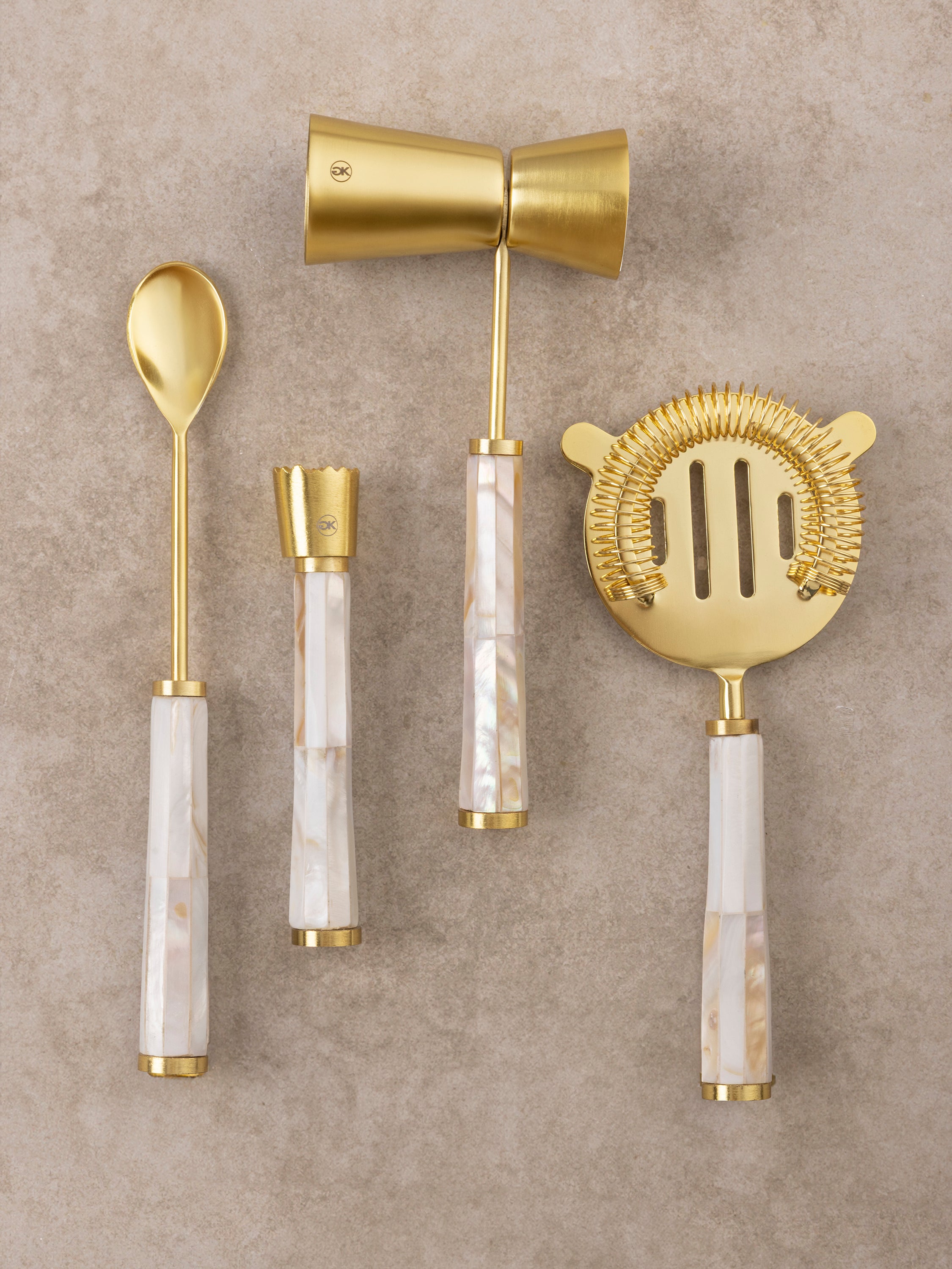 Bar tools set with brass-toned utensils and luminous mother of pearl handles shown in a clean top-down composition