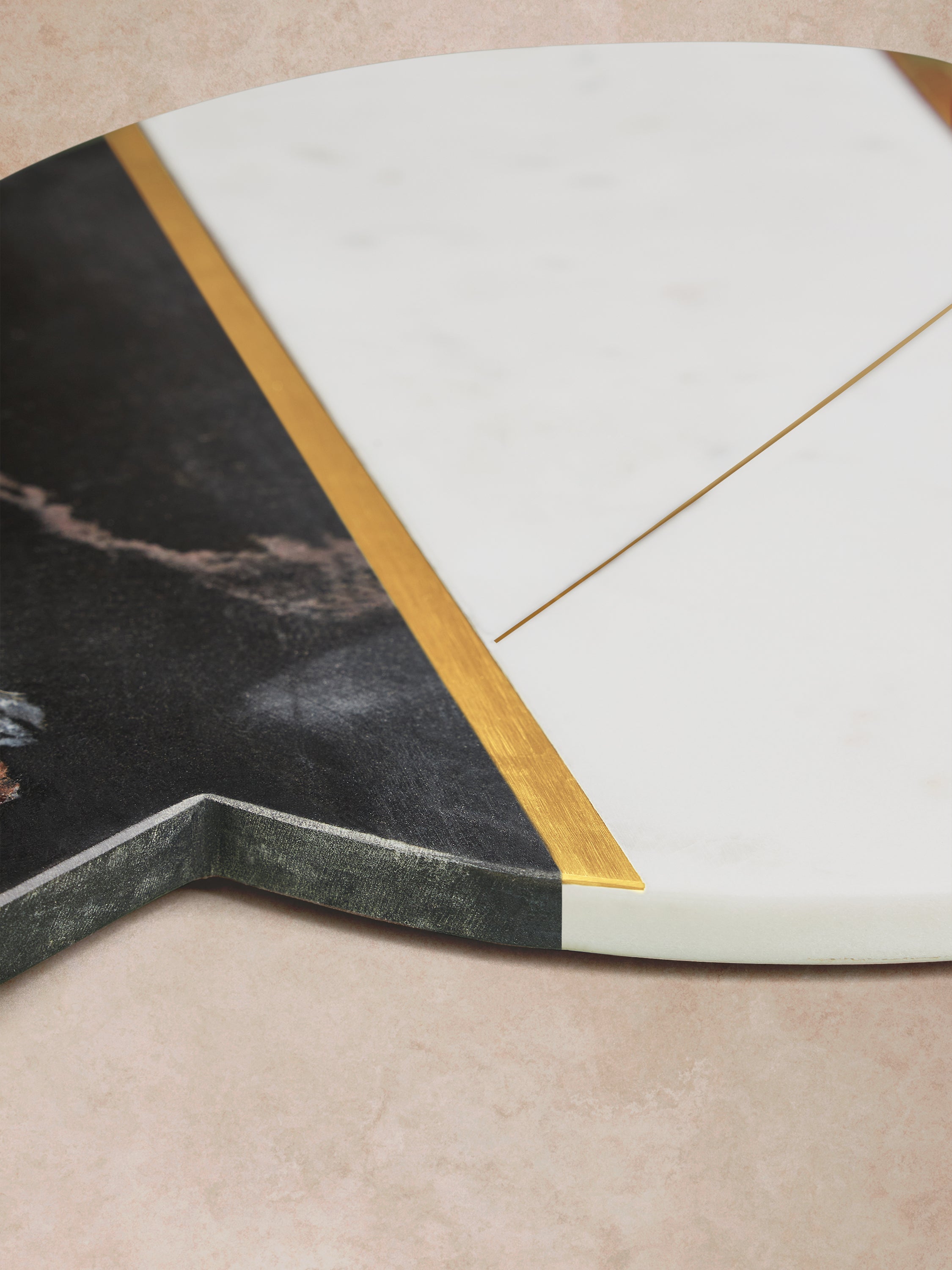 Close-up of marble board showing angular transitions between contrasting stone sections, thin brass inlay lines, and smooth beveled edge with natural veining