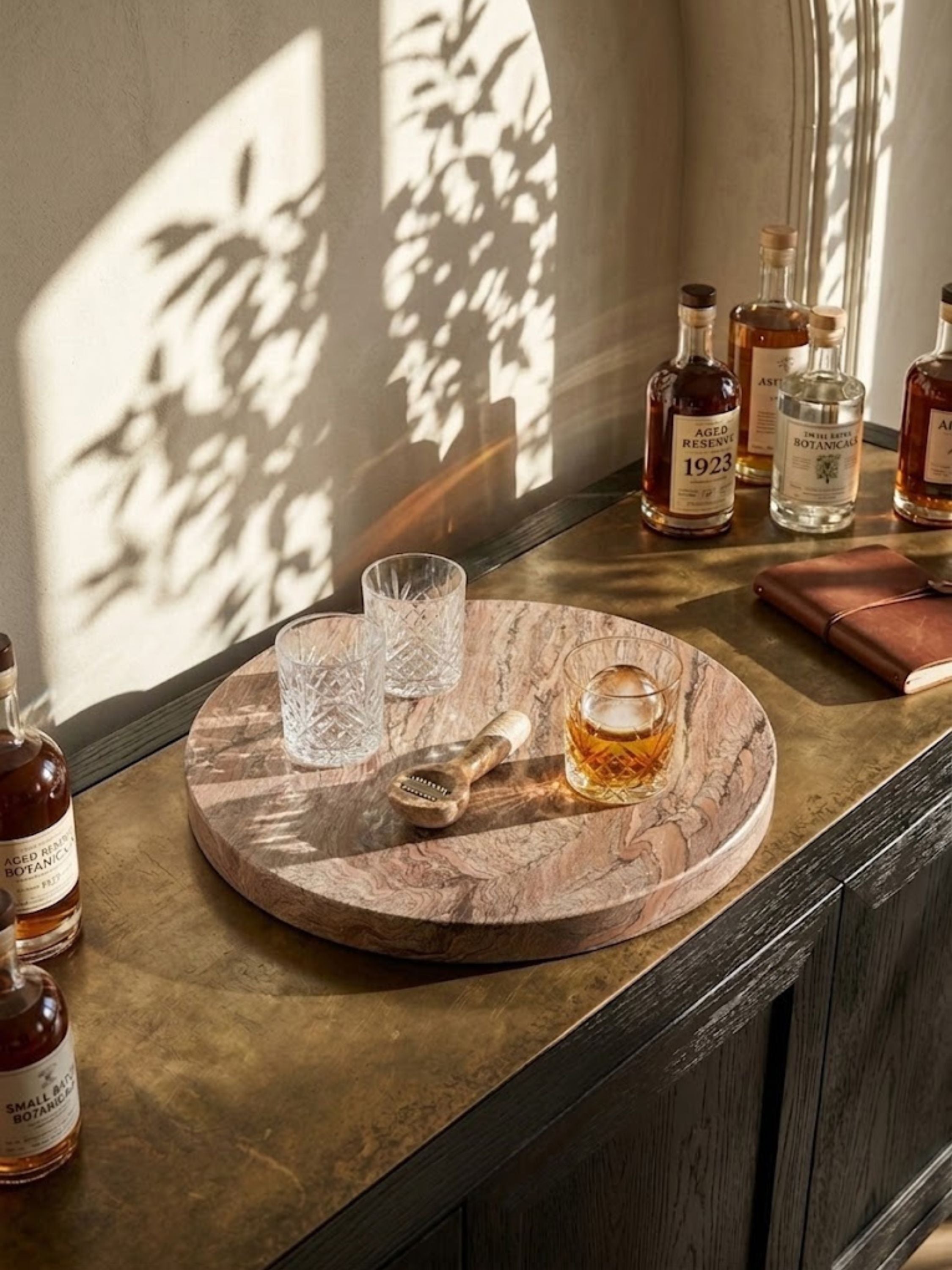 Ikoy brown onyx round tray arranged as a barware surface, paired with crystal glassware and bottles of spirits.