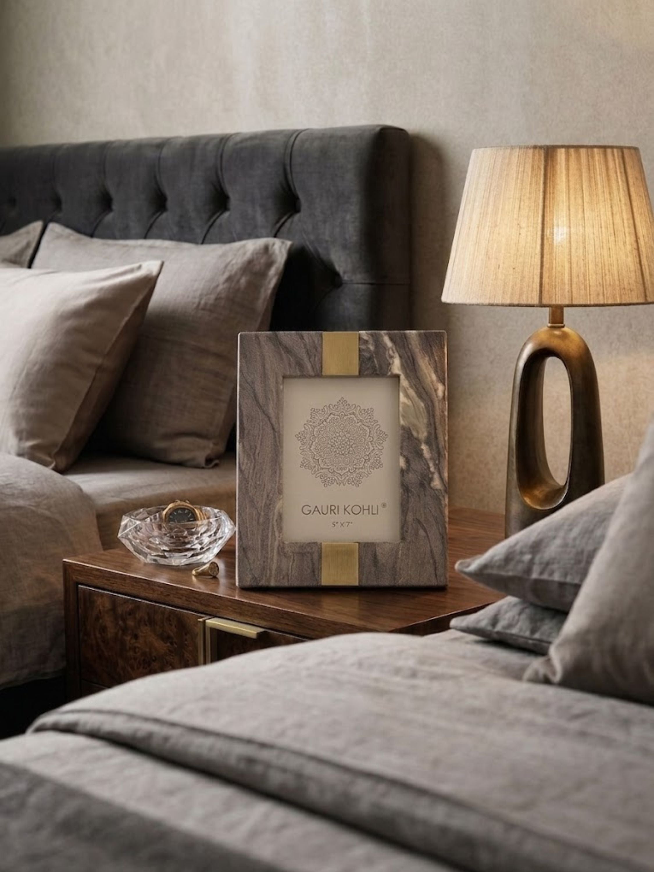 Skye brown onyx picture frame styled on a bedside table beside layered linen bedding and a sculptural lamp, showcasing the stone’s natural movement and refined presence.