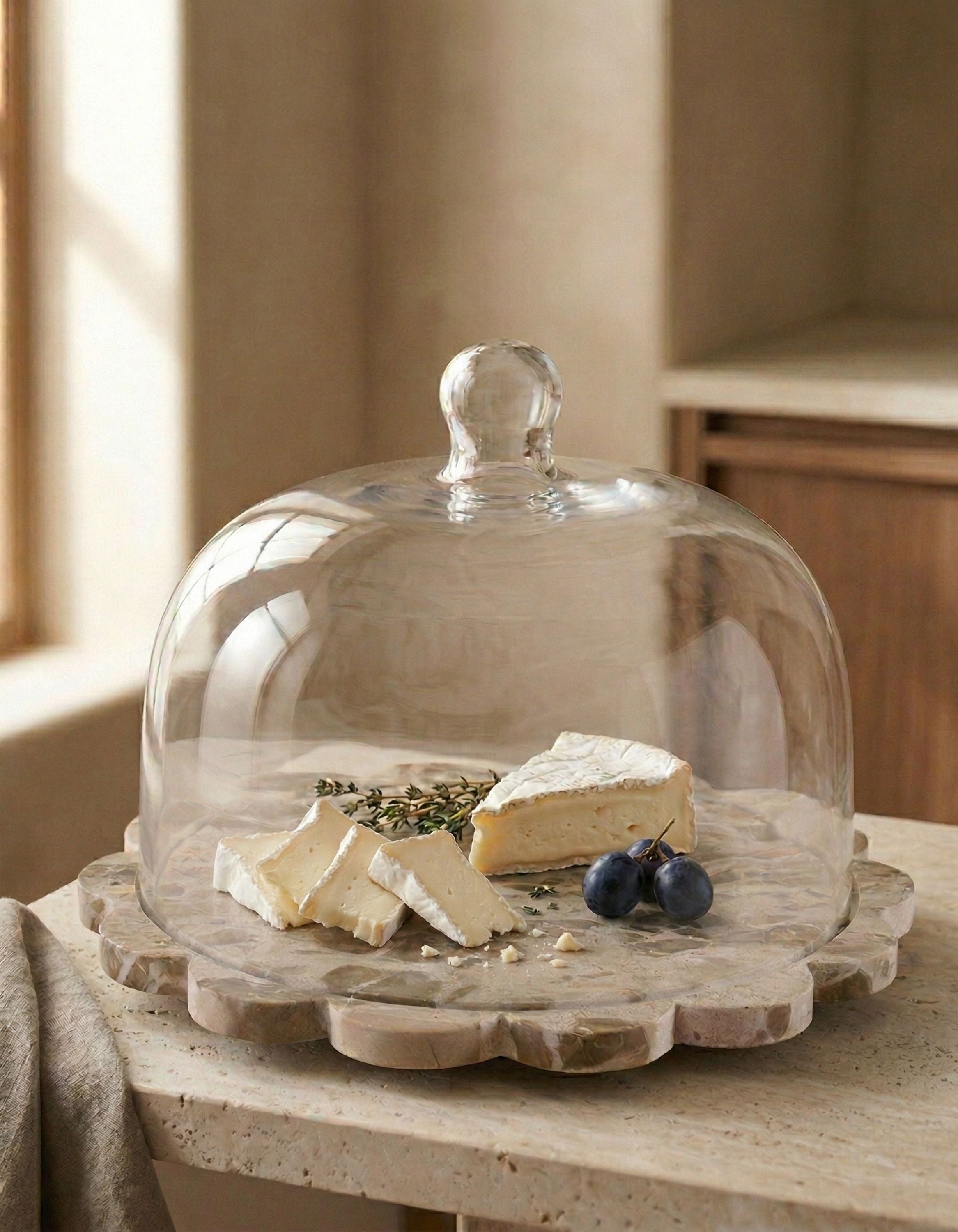 Onyx serving board with glass cloche covering cheese and fruit, styled on a tabletop in a warm, refined setting