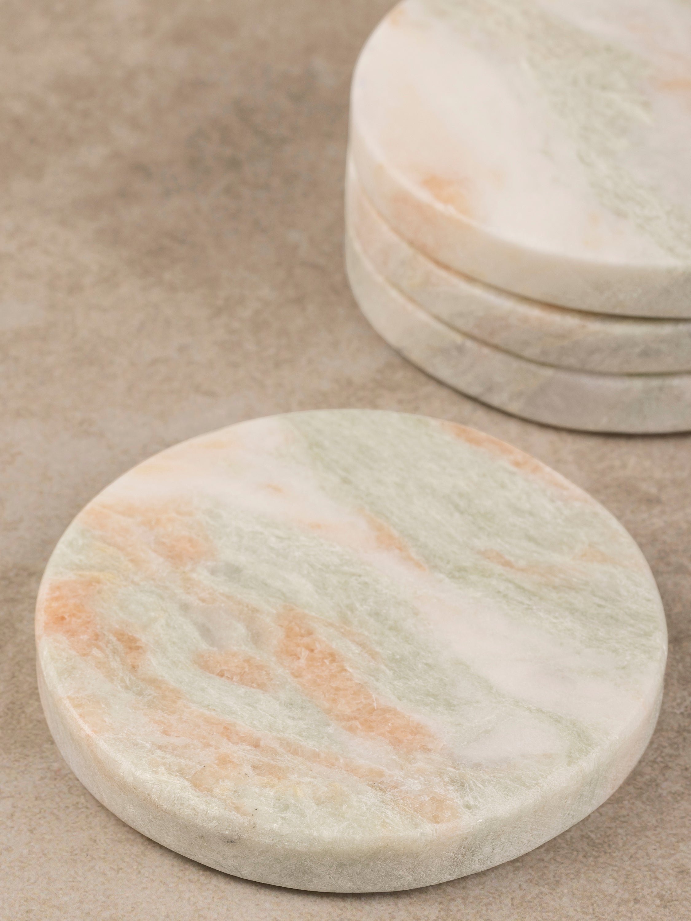 Close-up of stacked Moonlight onyx coasters showing layered green and ivory veining and the polished edge profile.