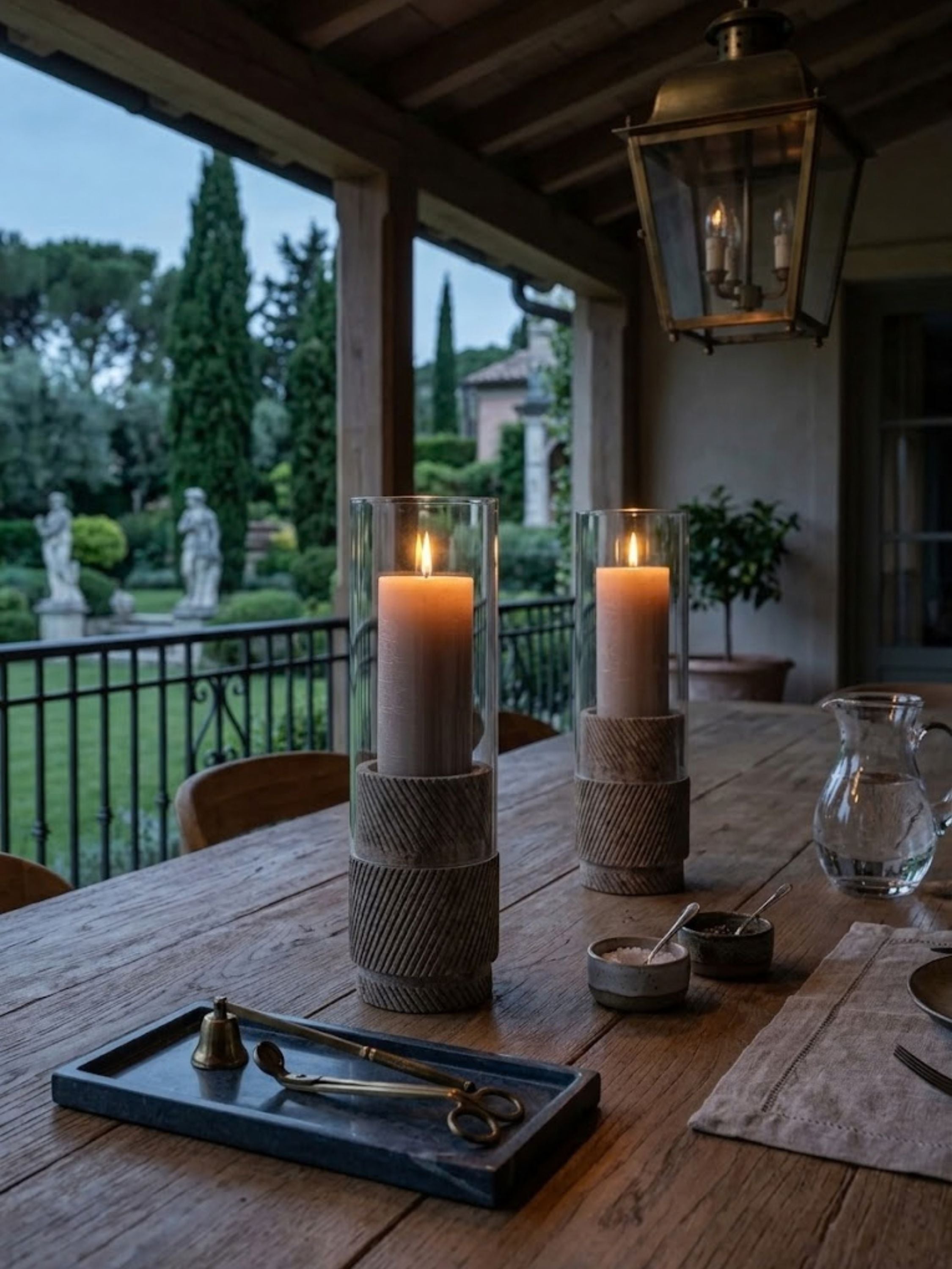 Estonia Brown Travertine hurricane candle holders displayed on a covered patio dining table, offering inviting candlelit atmosphere and natural stone texture for outdoor entertaining.