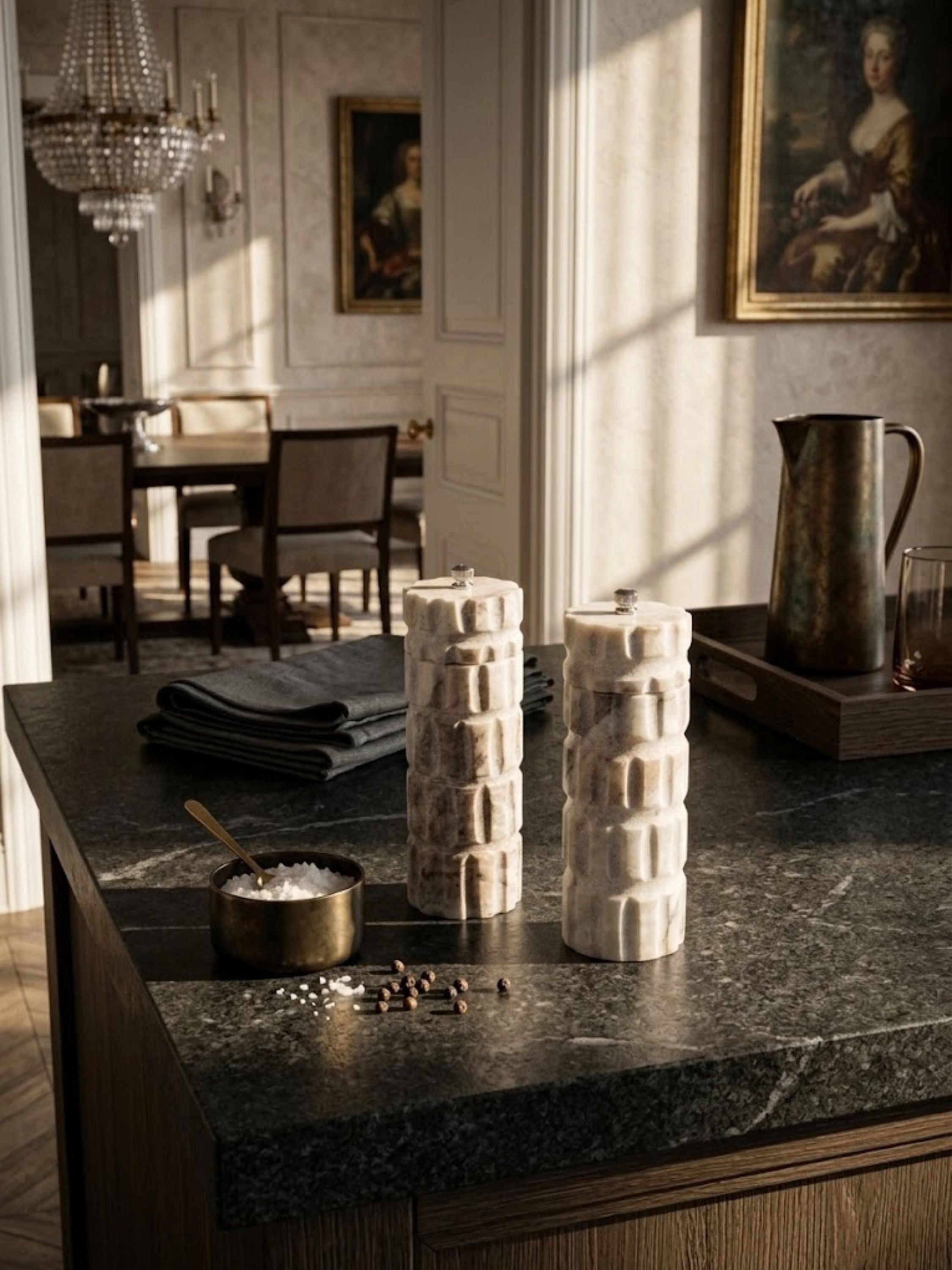 Beatrix Marble salt and pepper set displayed on a dark stone kitchen island with artisanal tableware, showcasing sculptural form and natural marble character.