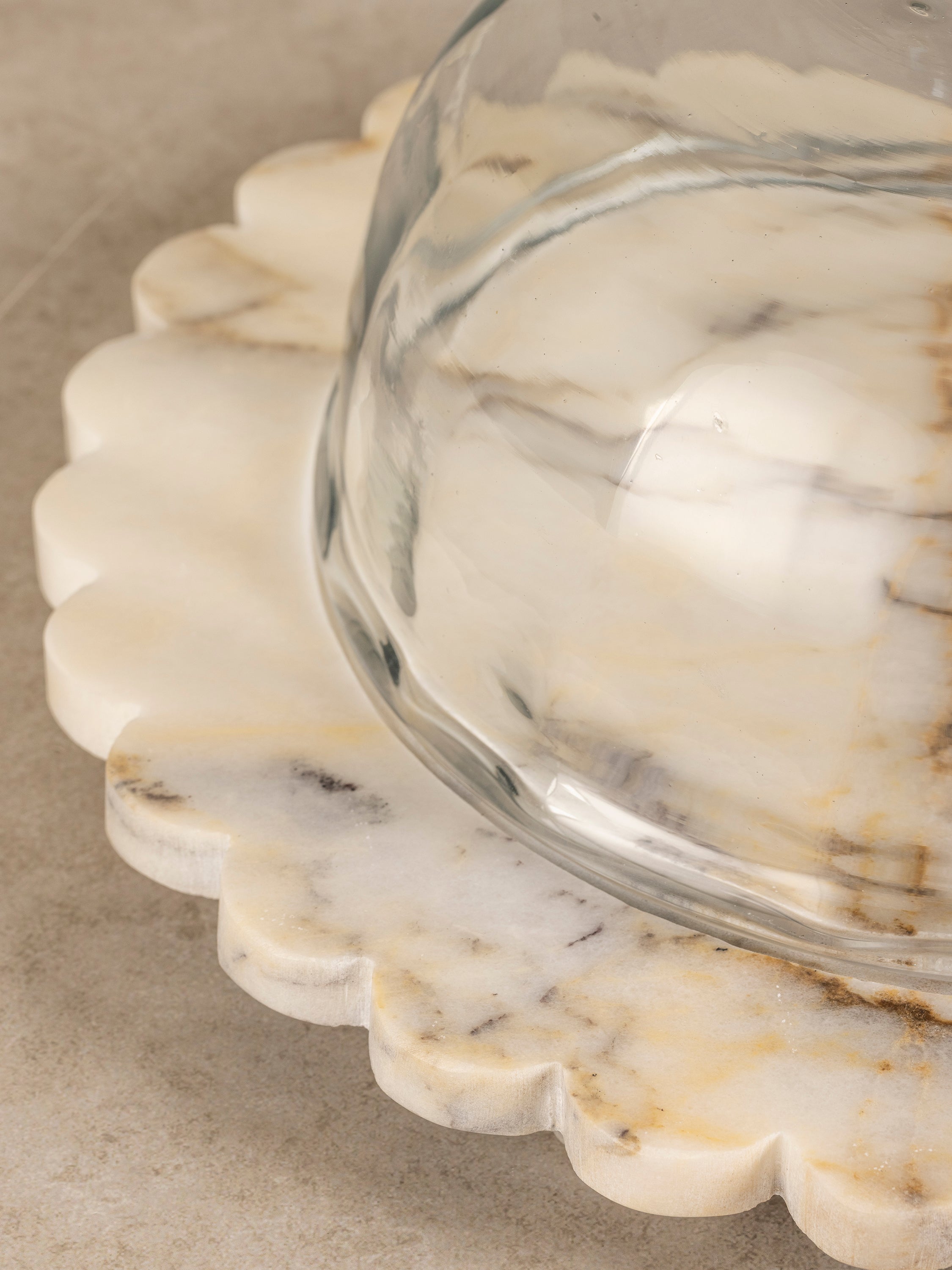 Close-up of Kismet scalloped onyx cheese board edge showing carved contours and layered natural stone veining beneath the glass dome