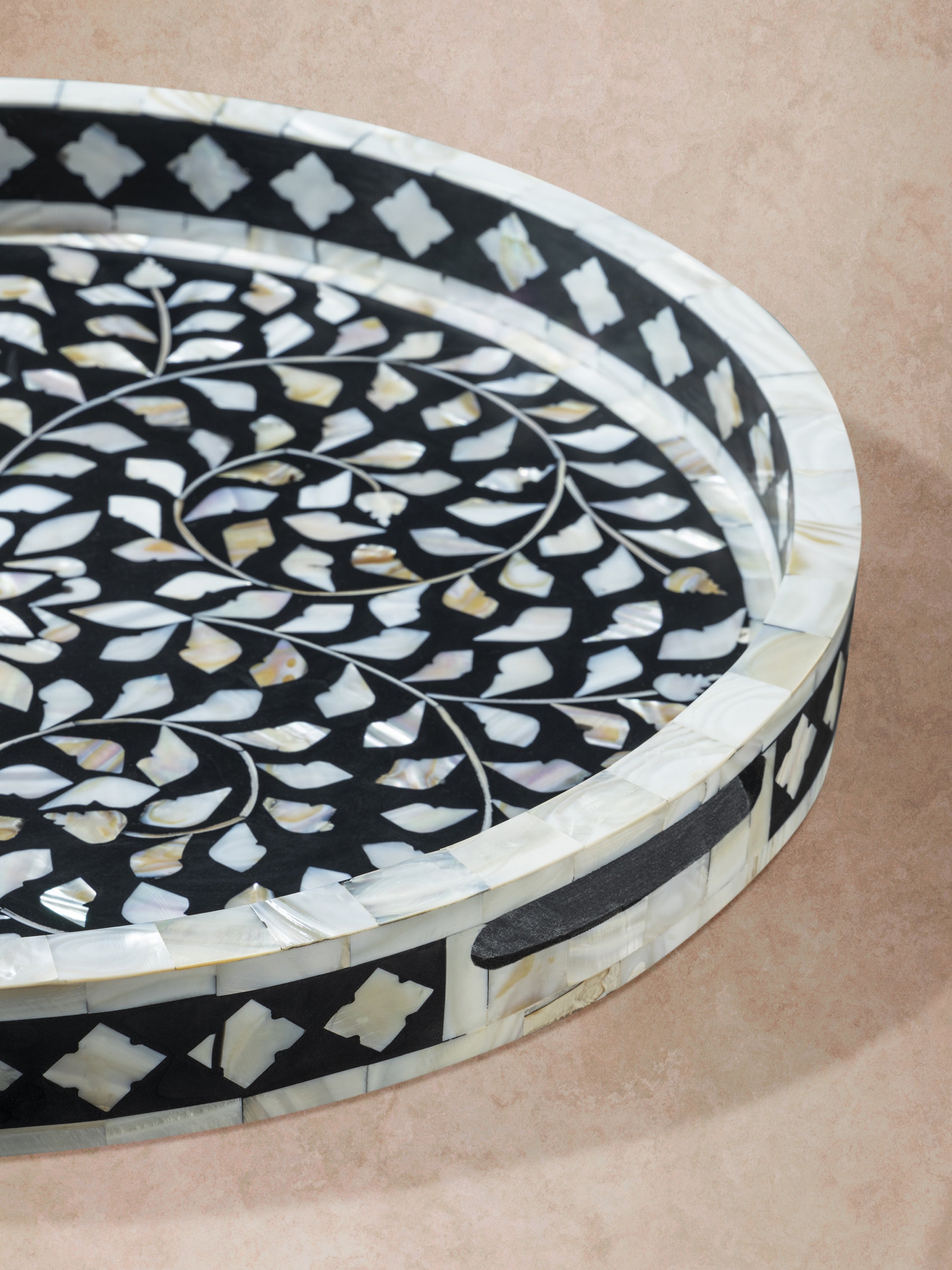Close-up angled view of black inlay tray showing raised rim, integrated handles, and continuous vine pattern across the surface