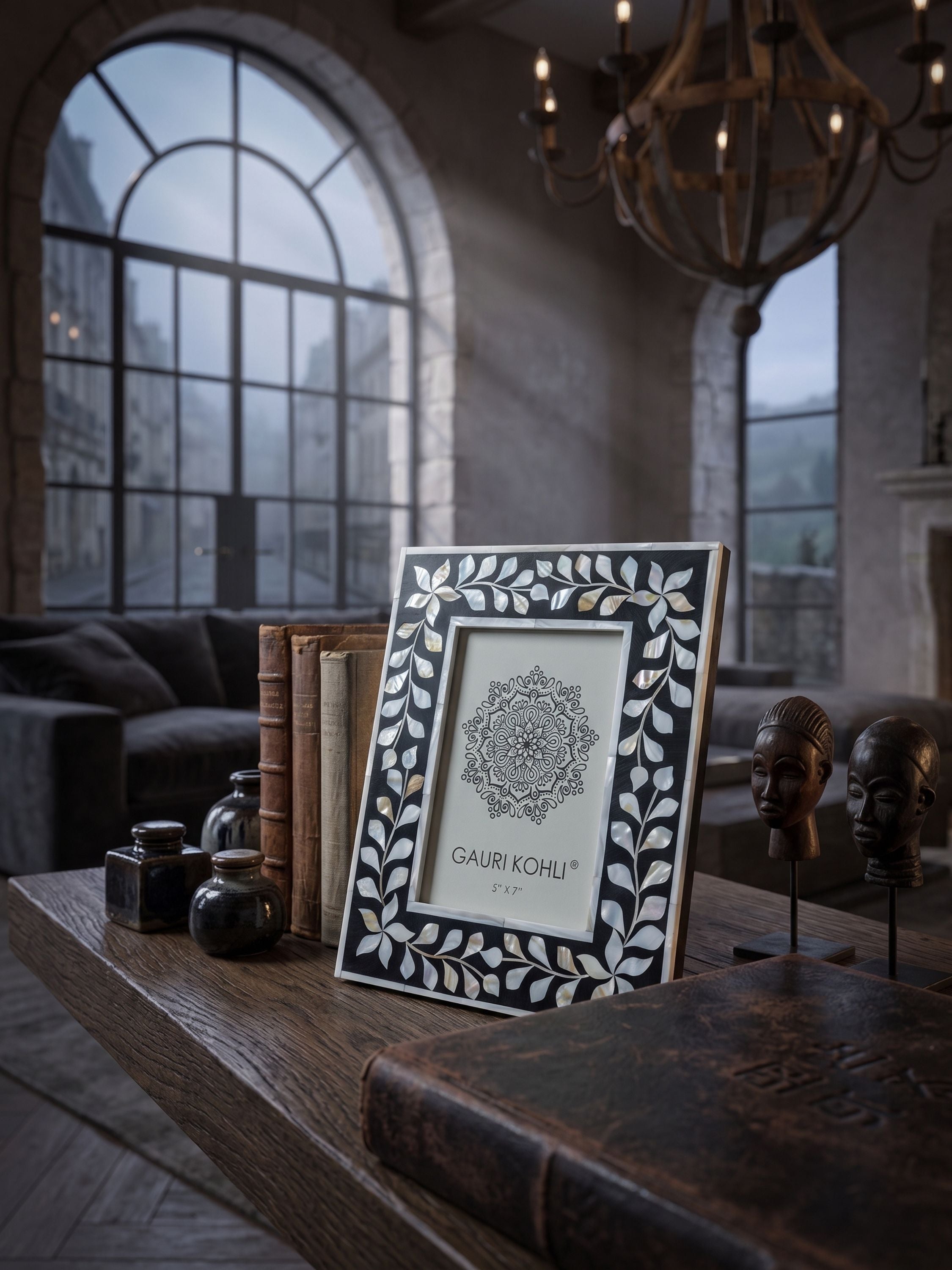 Black mother of pearl inlay picture frame with botanical vine pattern, placed on a wooden surface with books and objects in a warm interior setting