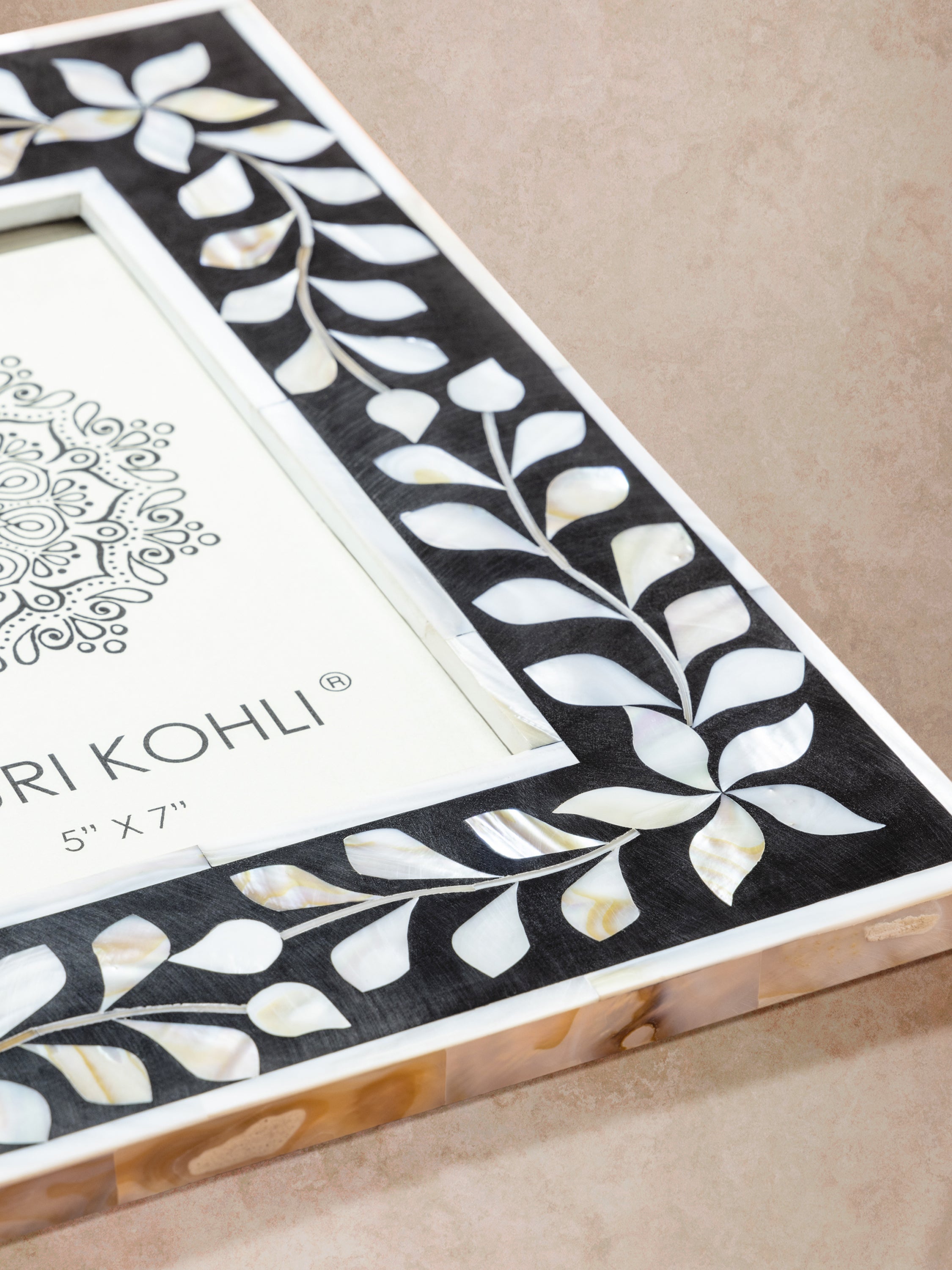 Close-up of picture frame corner showing bone inlay vine pattern, smooth polished finish, and contrast between dark resin and light inlay
