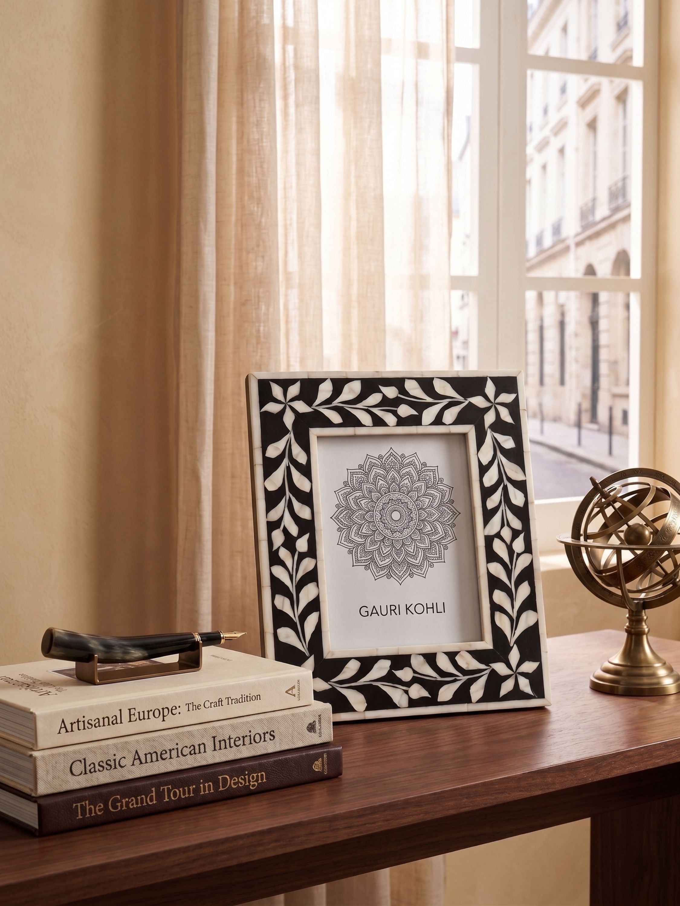 Bone inlay black tabletop photo frame with vine border design styled on a wooden console with books and decorative accents near a window