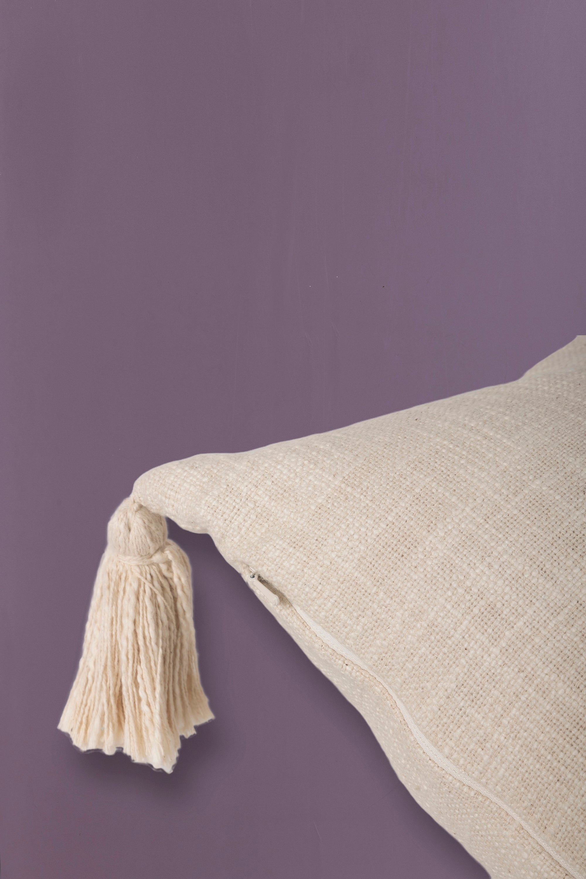 Handwoven neutral-colored square cushion with stylish tassel accents on each corner