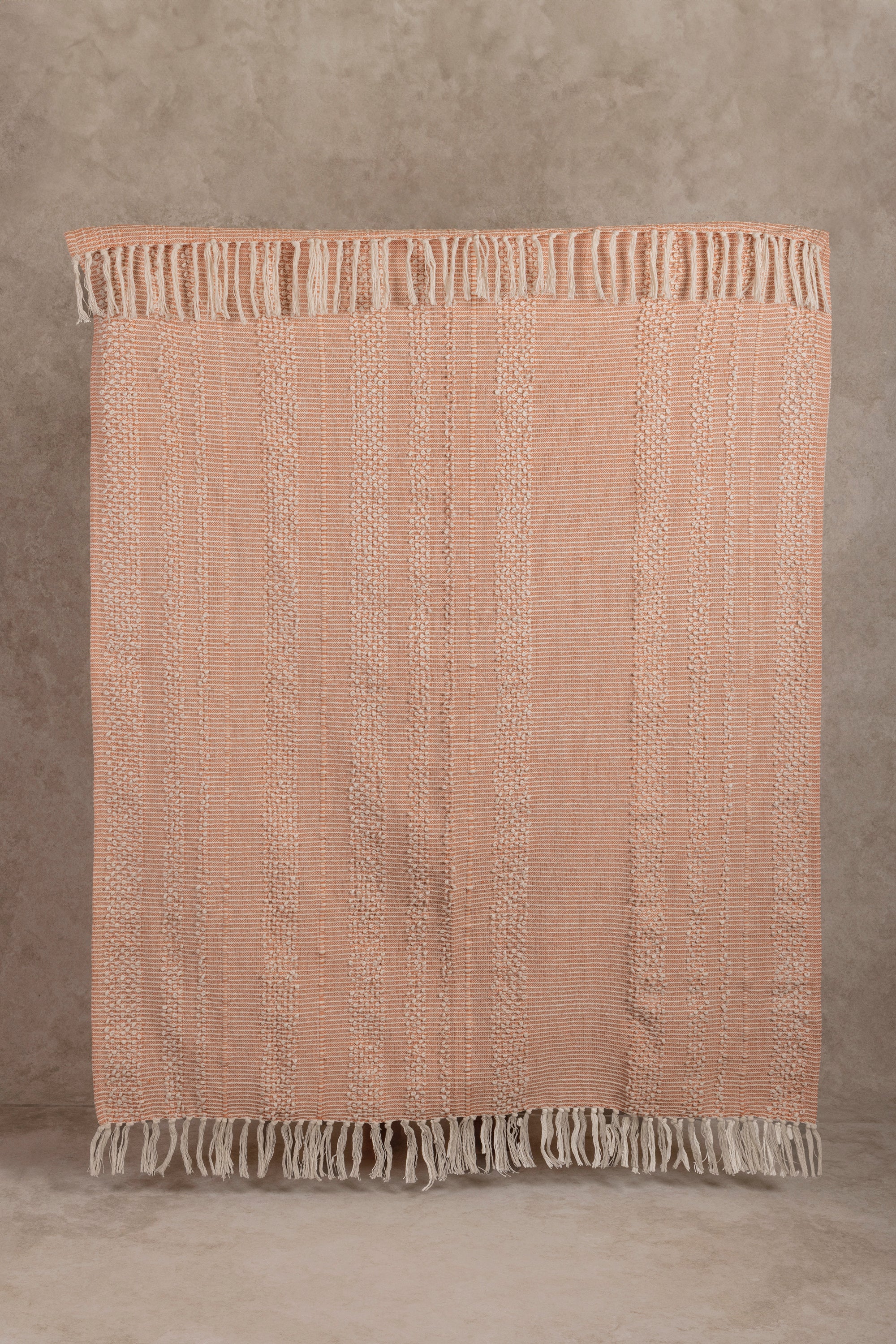 Soft peach pink striped cotton throw blanket with delicate woven texture and tassel fringe, perfect for cozy home decor