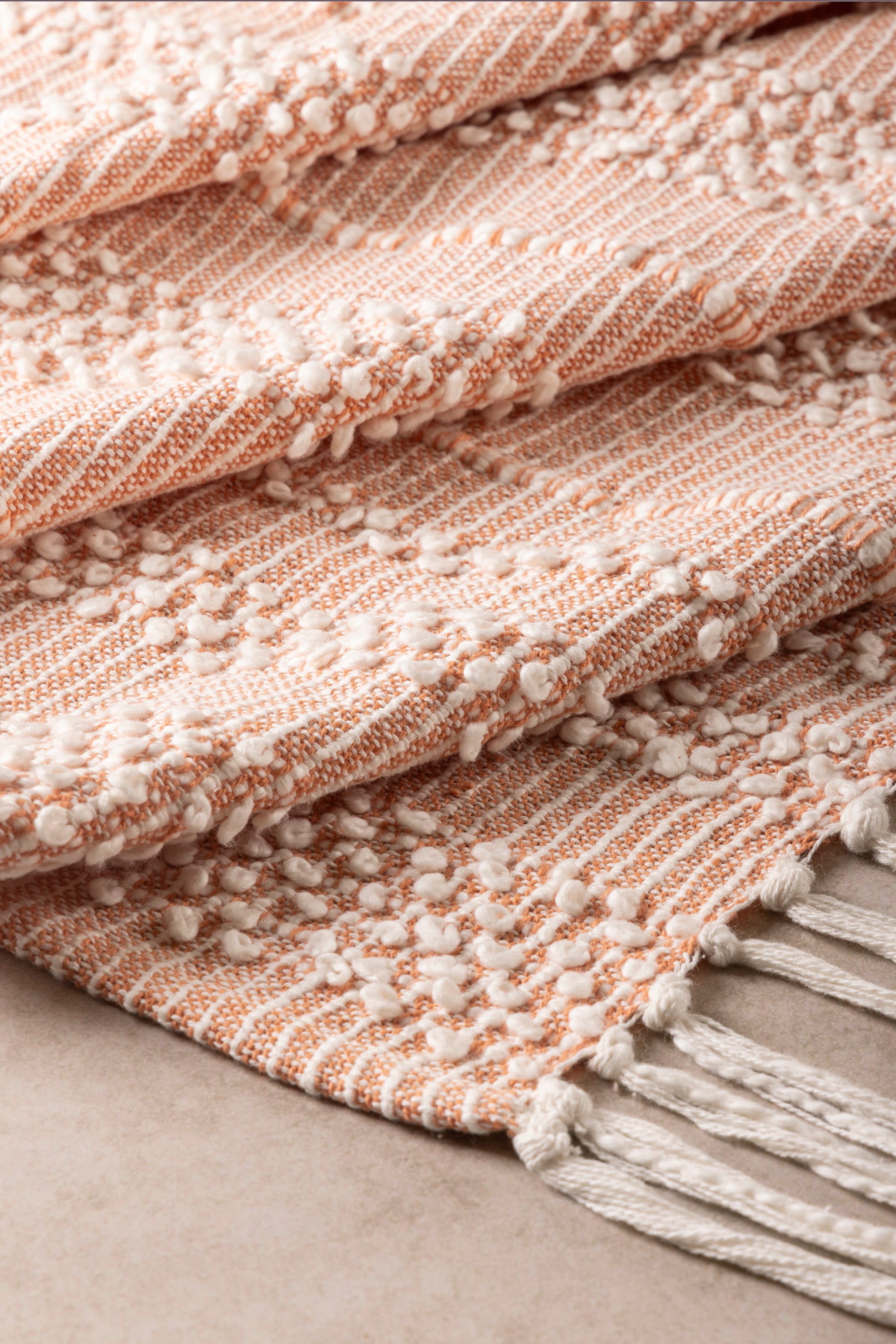 Soft peach pink striped cotton throw blanket with delicate woven texture and tassel fringe, perfect for cozy home decor