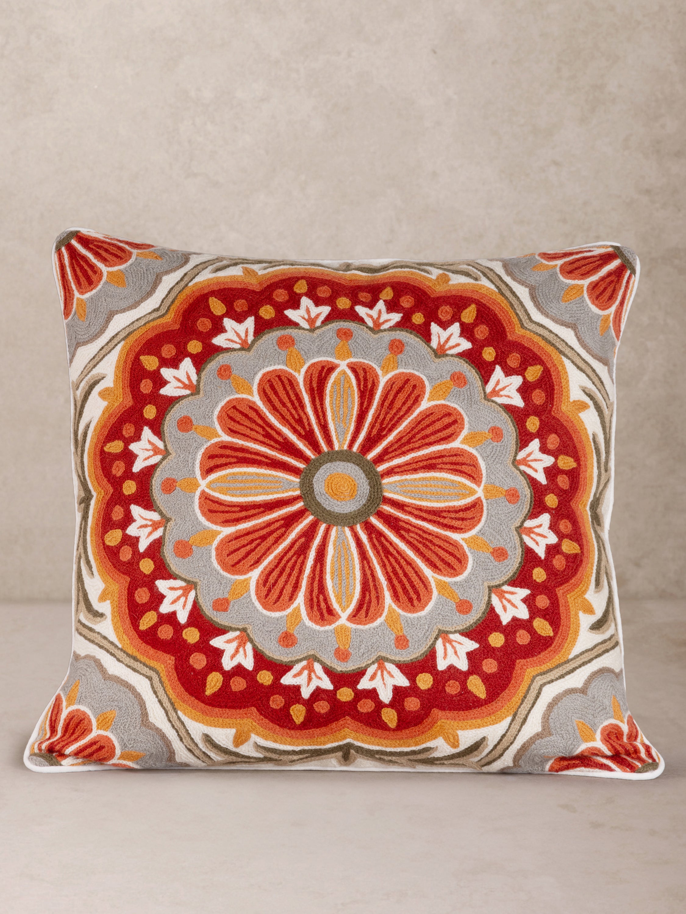 Elegant embroidered throw pillow featuring a detailed mandala-inspired floral design in warm tones of red, orange, and gray