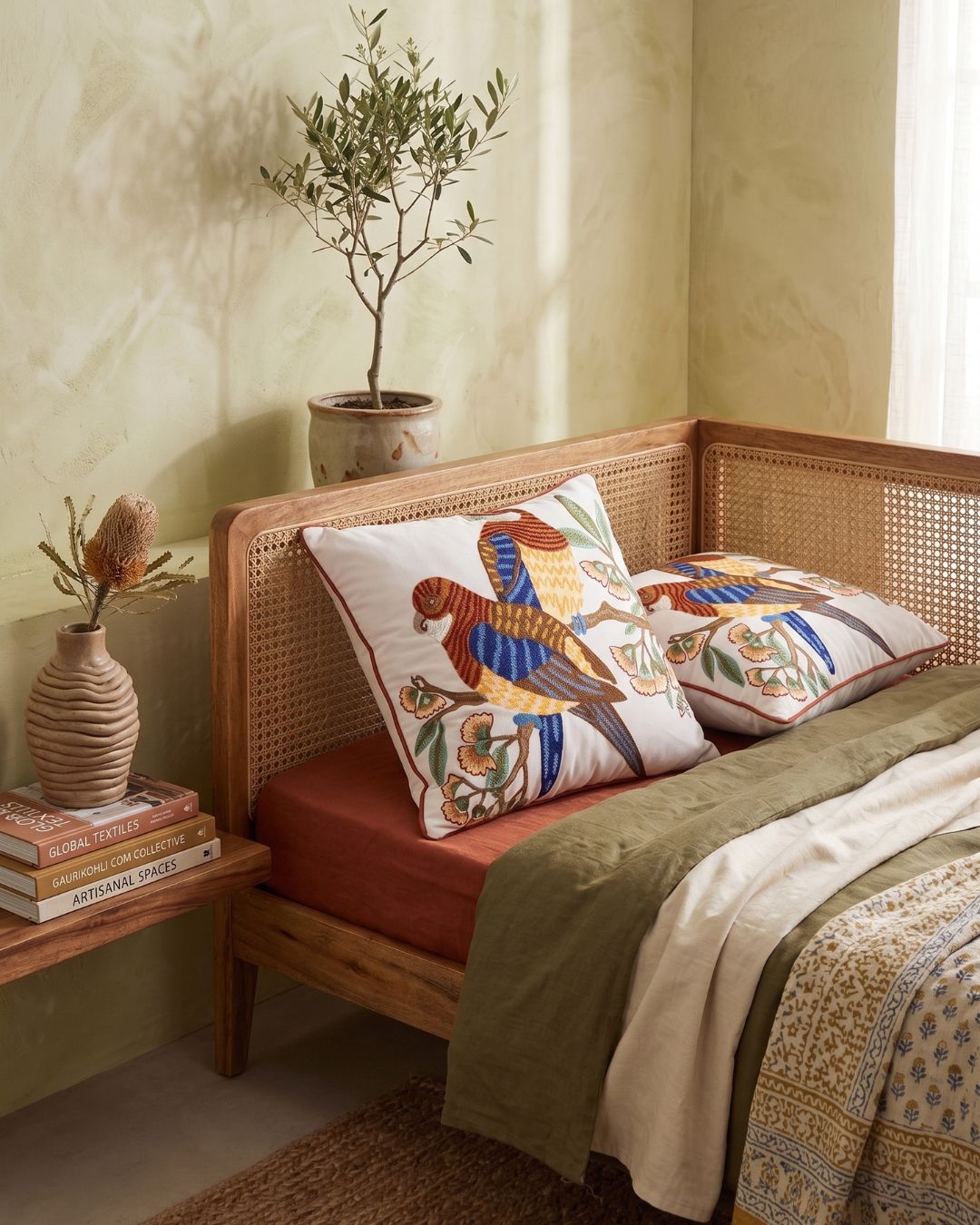 Hand embroidered bird motif pillow cover in multicolor thread on an ivory base styled on a wooden daybed with neutral textiles
