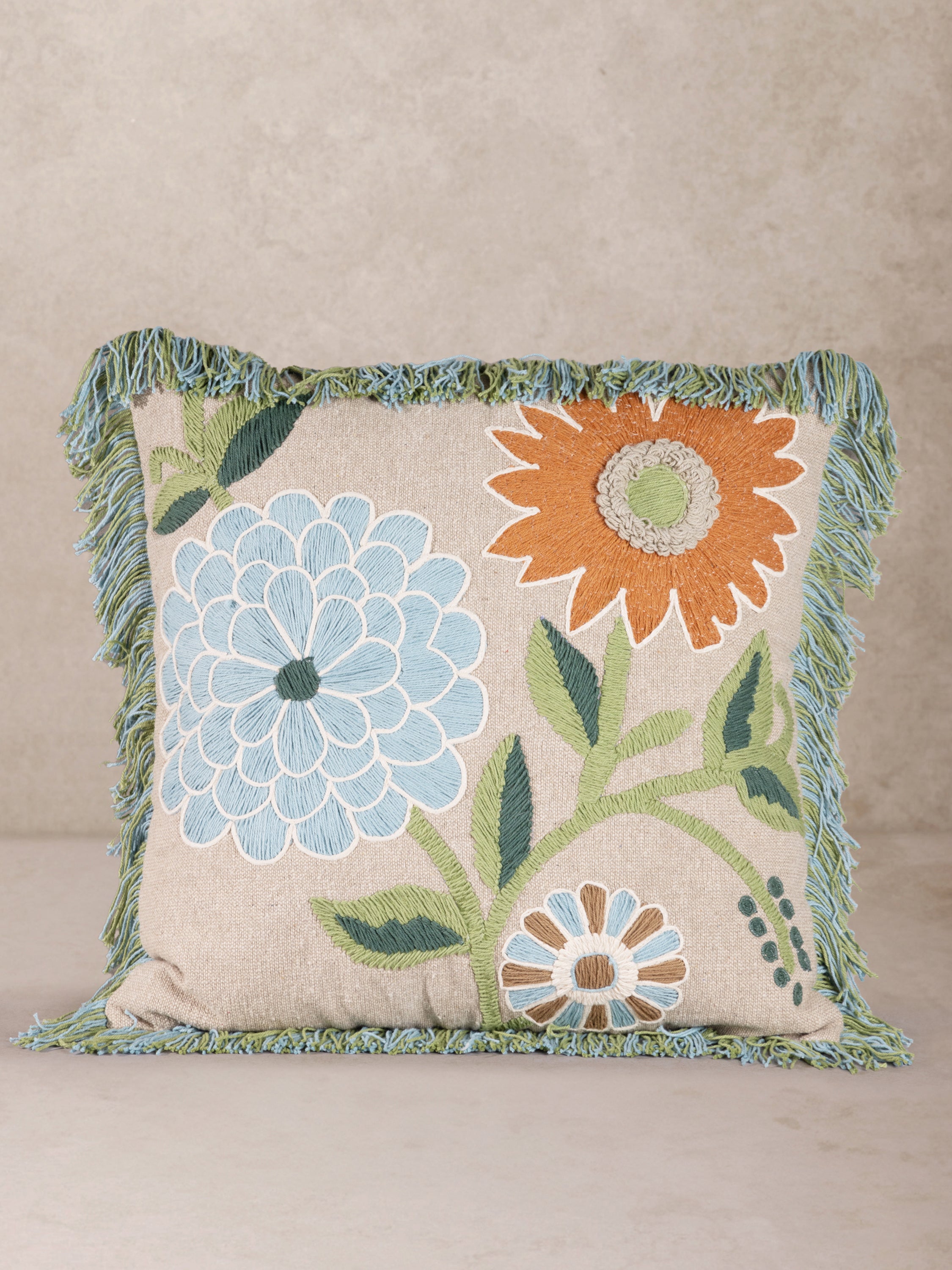 Embroidered Floral Throw Pillow with Green Fringe Trim – A beautifully handcrafted decorative pillow featuring intricate floral embroidery in soft blue, orange, and green hues with a textured fringe border