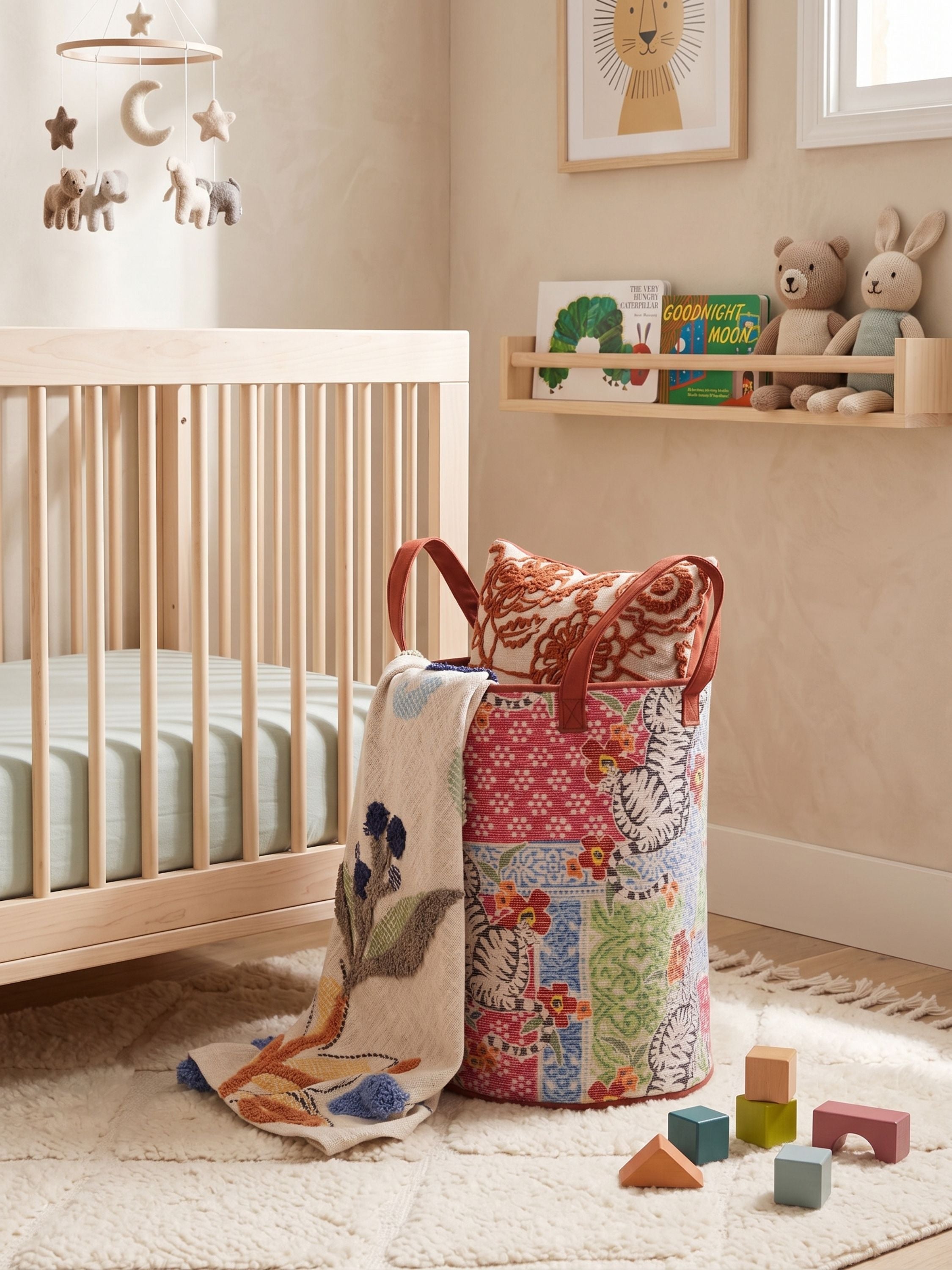 Printed canvas patchwork laundry basket in multicolor placed beside a crib in a nursery setting with soft toys and decor