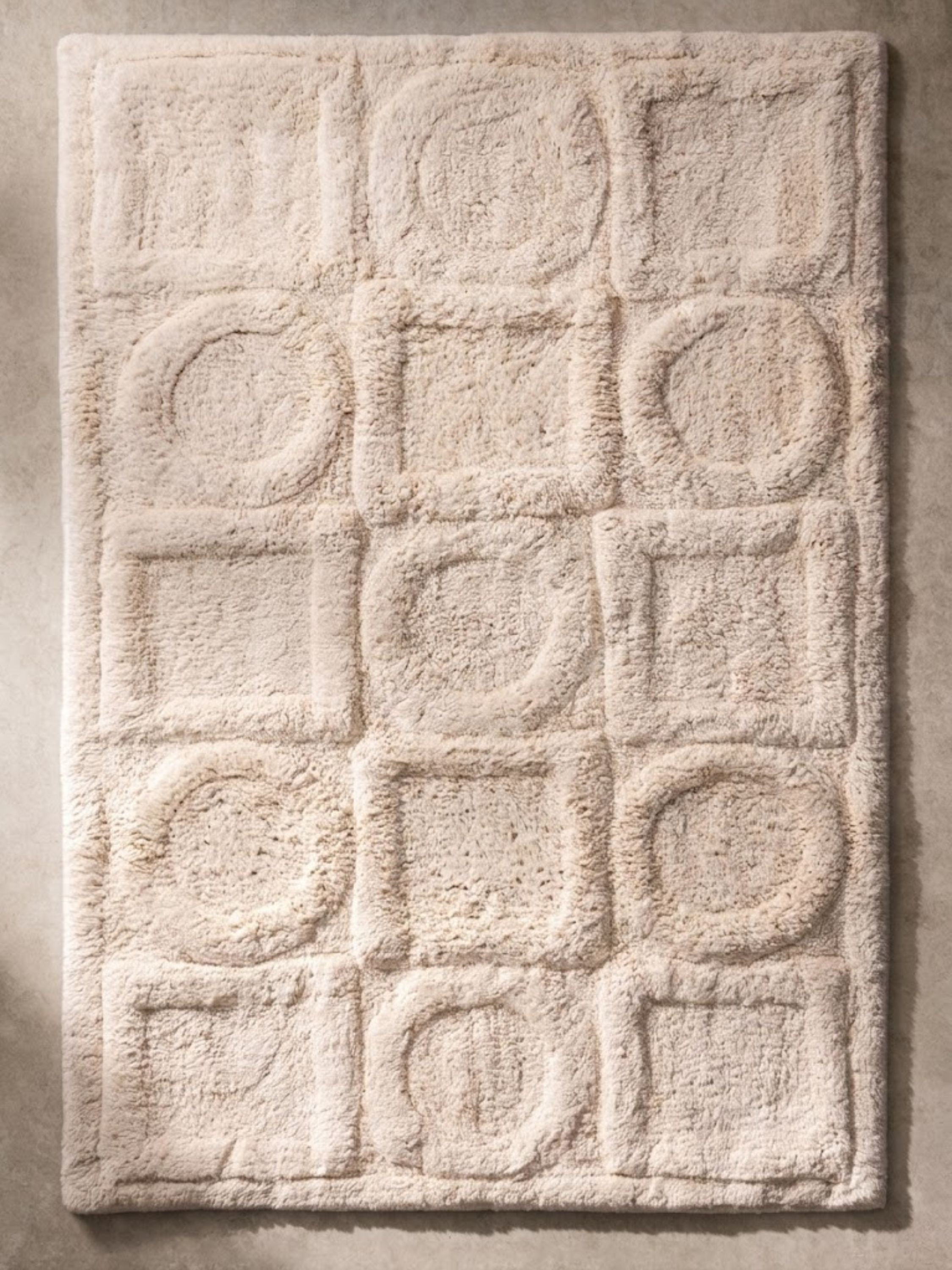 Ivory geometric bath mat featuring a sculpted grid of raised circles and squares, crafted in plush cotton texture to bring subtle dimension and spa-inspired softness to the bathroom.