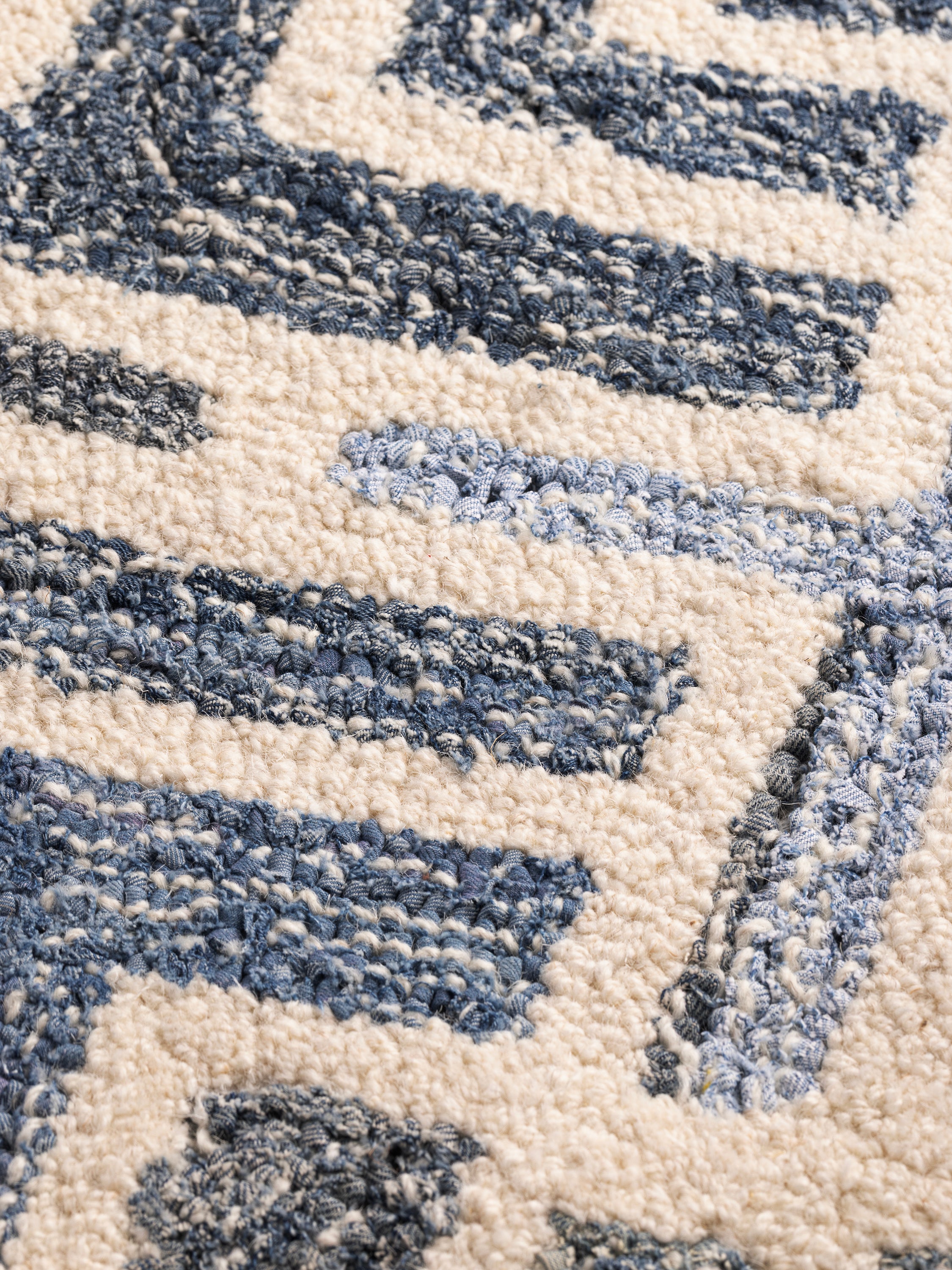 Close-up of hand-tufted Santorini rug showing wool and denim fibers with sculpted blue and ivory motifs