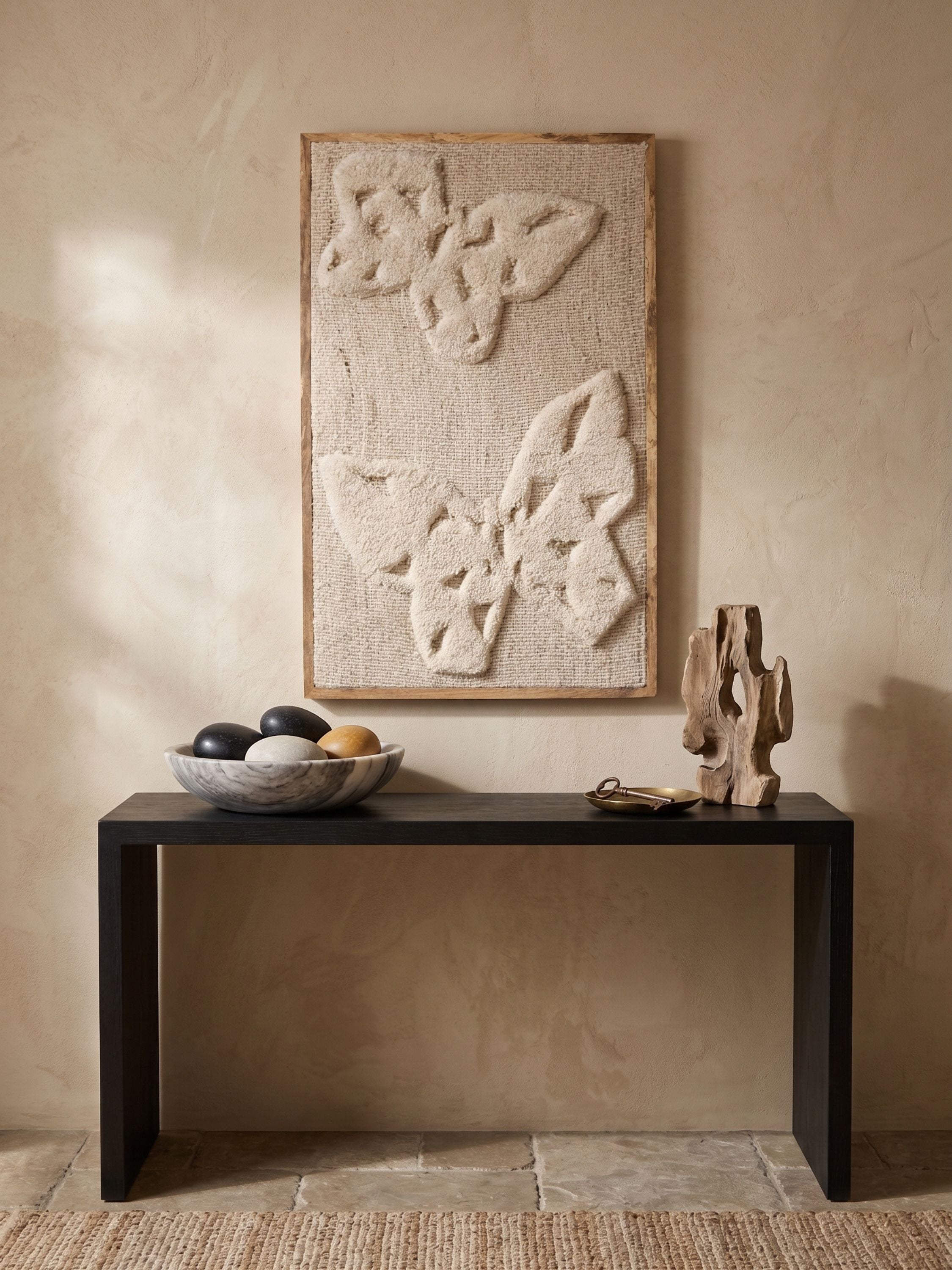 Ivory tufted wool wall art with sculpted botanical relief pattern, placed above a dark console table with decorative objects in a warm interior