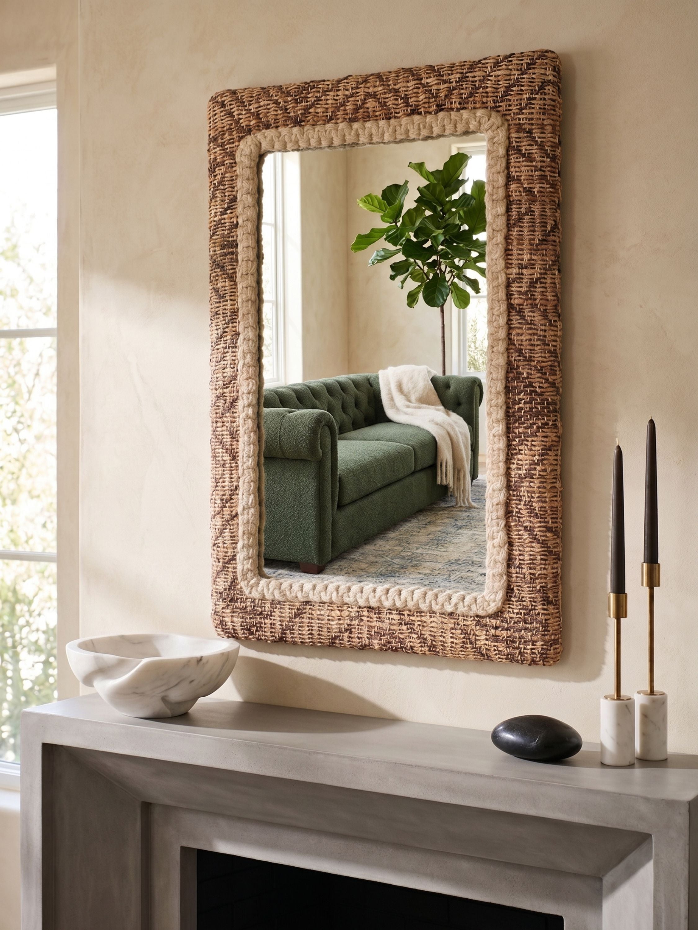Wall mirror with textured jute woven frame and braided inner detail in natural brown tones, styled above a mantel reflecting a living room setting