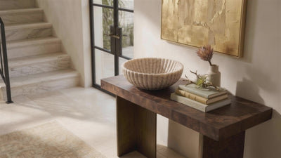 Beige onyx fluted bowl on a burl wood console in an entryway, the camera easing slowly toward it as leaf shadows drift across the plaster wall