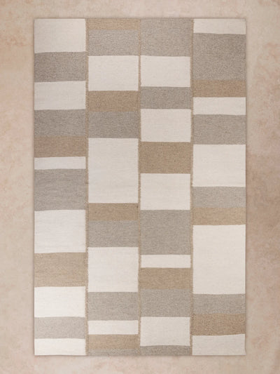 Handwoven area rug with tonal checkerboard pattern in warm beige and taupe tones shown in motion, with shifting light revealing subtle pile variation, block transitions, and surface depth