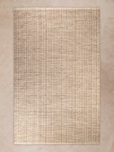 Handwoven area rug in natural beige tones shown in motion, with shifting light revealing dense woven texture, fine linear patterning, and subtle tonal variation